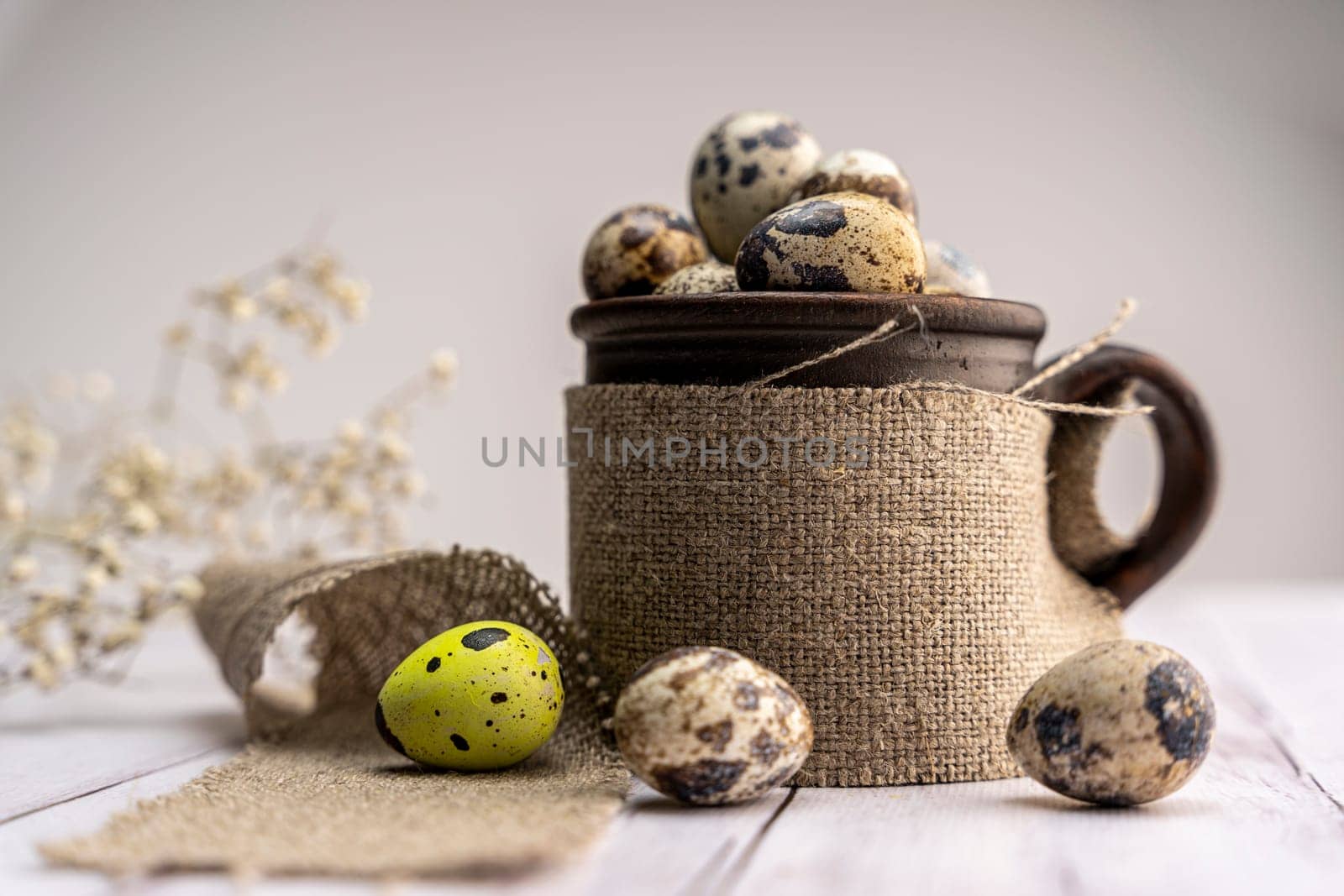 Fresh quail eggs in a clay mug on the table. Bright spring festive background and a branch of gypsophila. Close-up. Healthy eating. Easter.