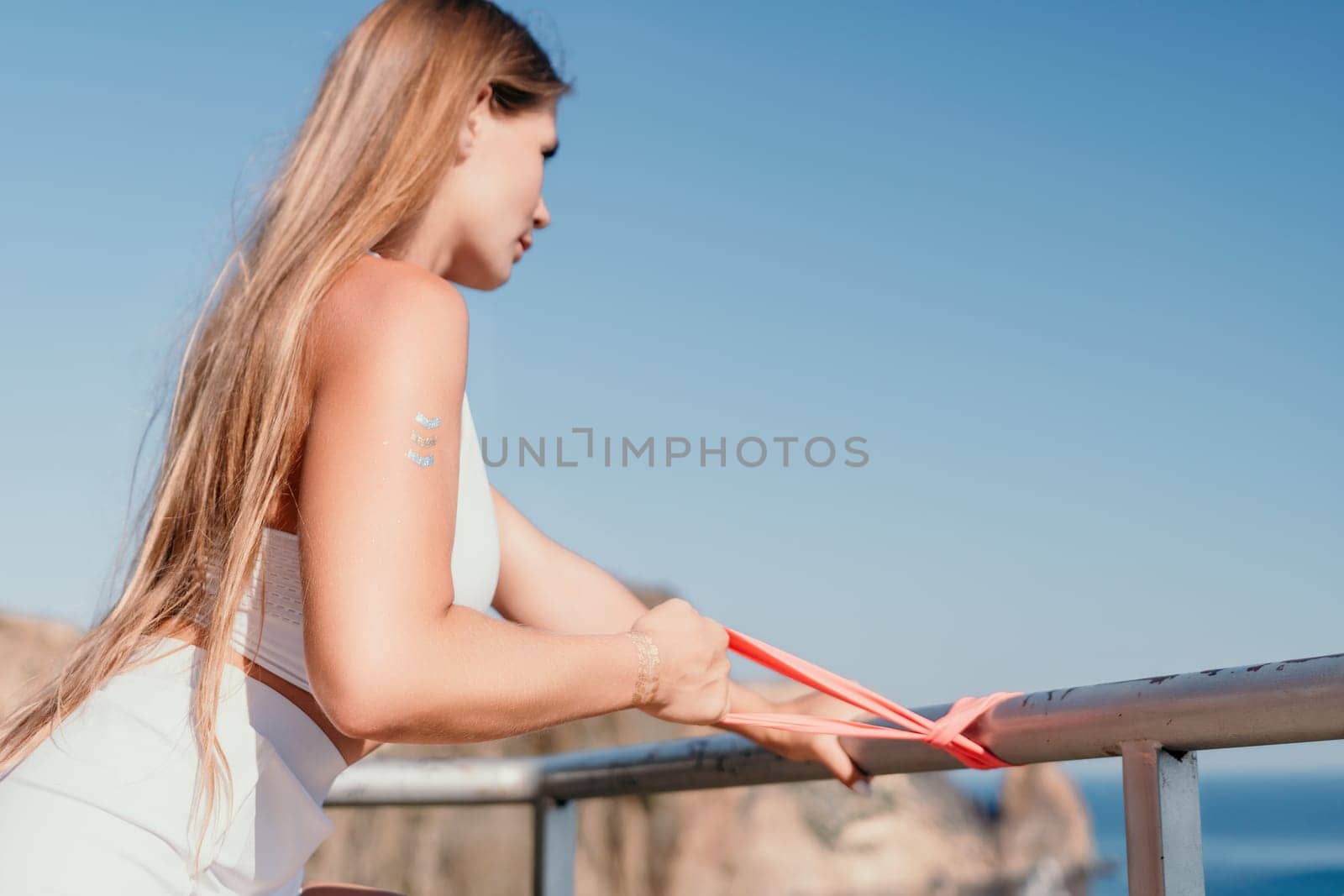 Woman sea fitness. Happy woman with long hair, fitness instructor in white doing stretching and pilates with ribbons in park near the sea. Female fitness yoga routine concept. Healthy lifestyle. by panophotograph