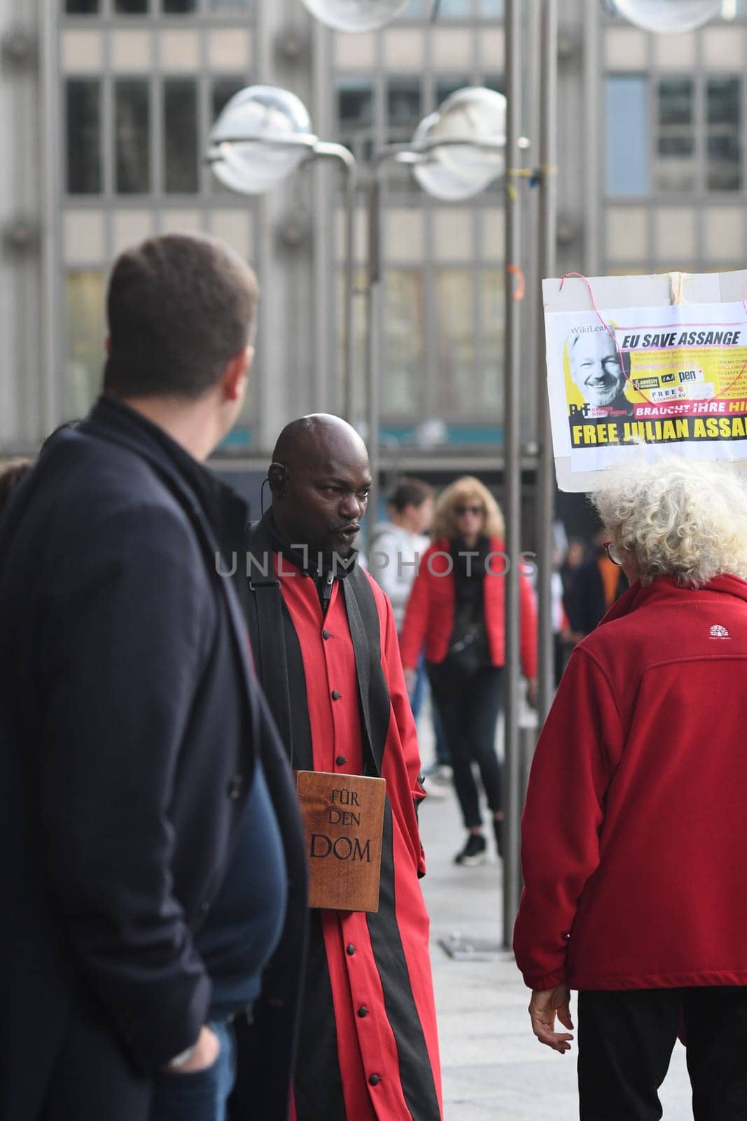 Vertical shot of the Cathedral servant in front of Cologne Cathedral in a red robe arguing with a Free Assange demonstrant, Cologne, Germany