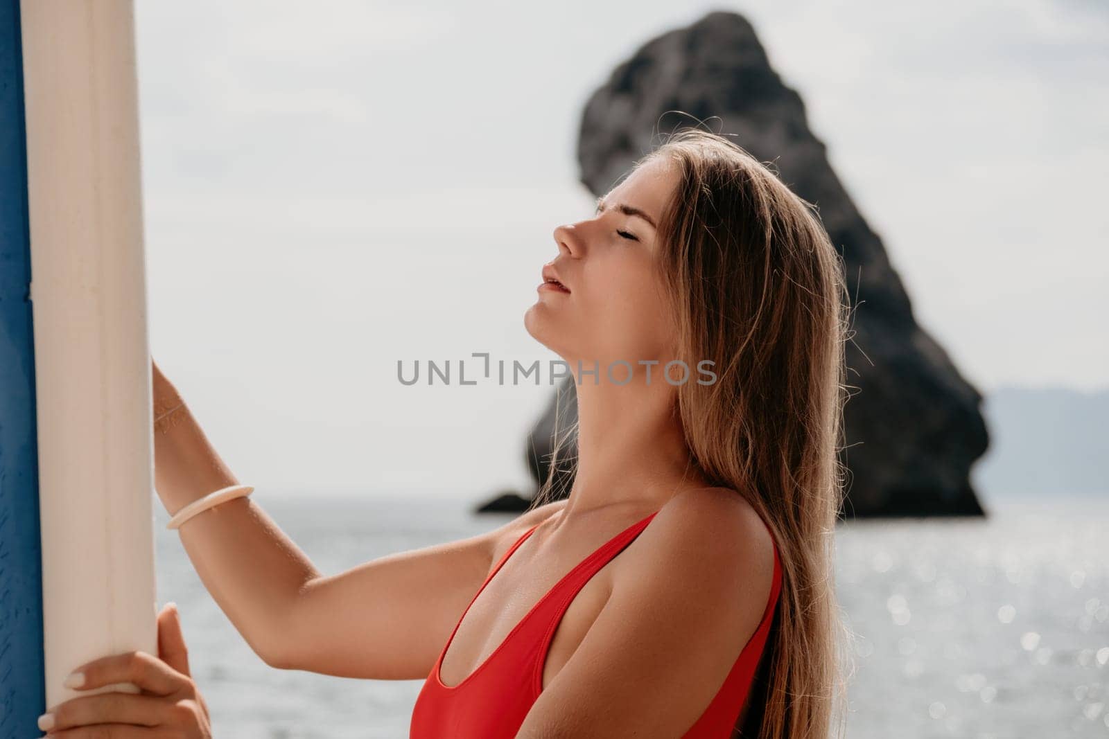 Close up shot of beautiful young caucasian woman with black hair and freckles looking at camera and smiling. Cute woman portrait in a pink bikini posing on a volcanic rock high above the sea