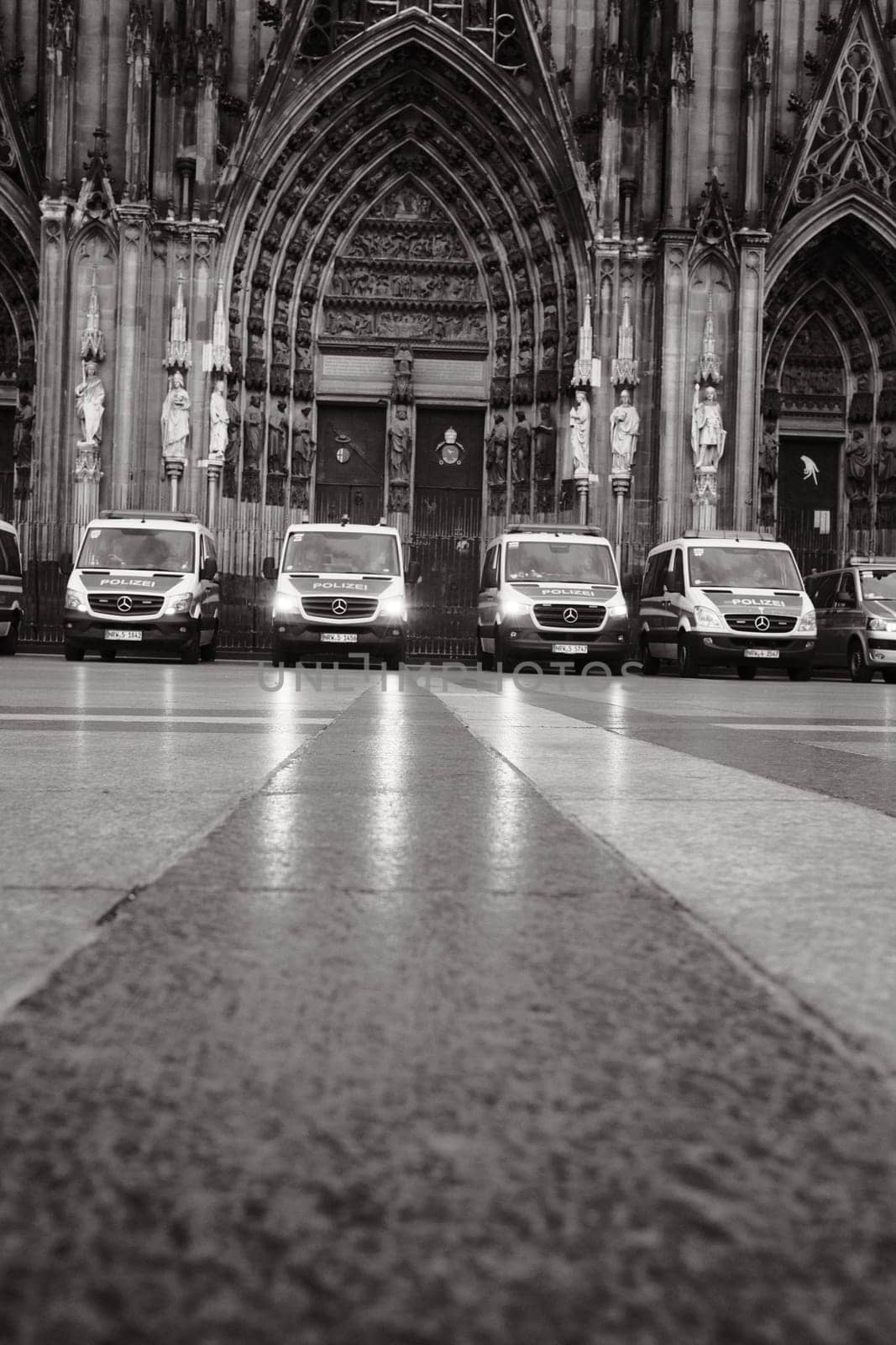 Grayscale shot of row of Mercedes-Benz Sprinter police cars in front of Cologne Cathedral in Germany