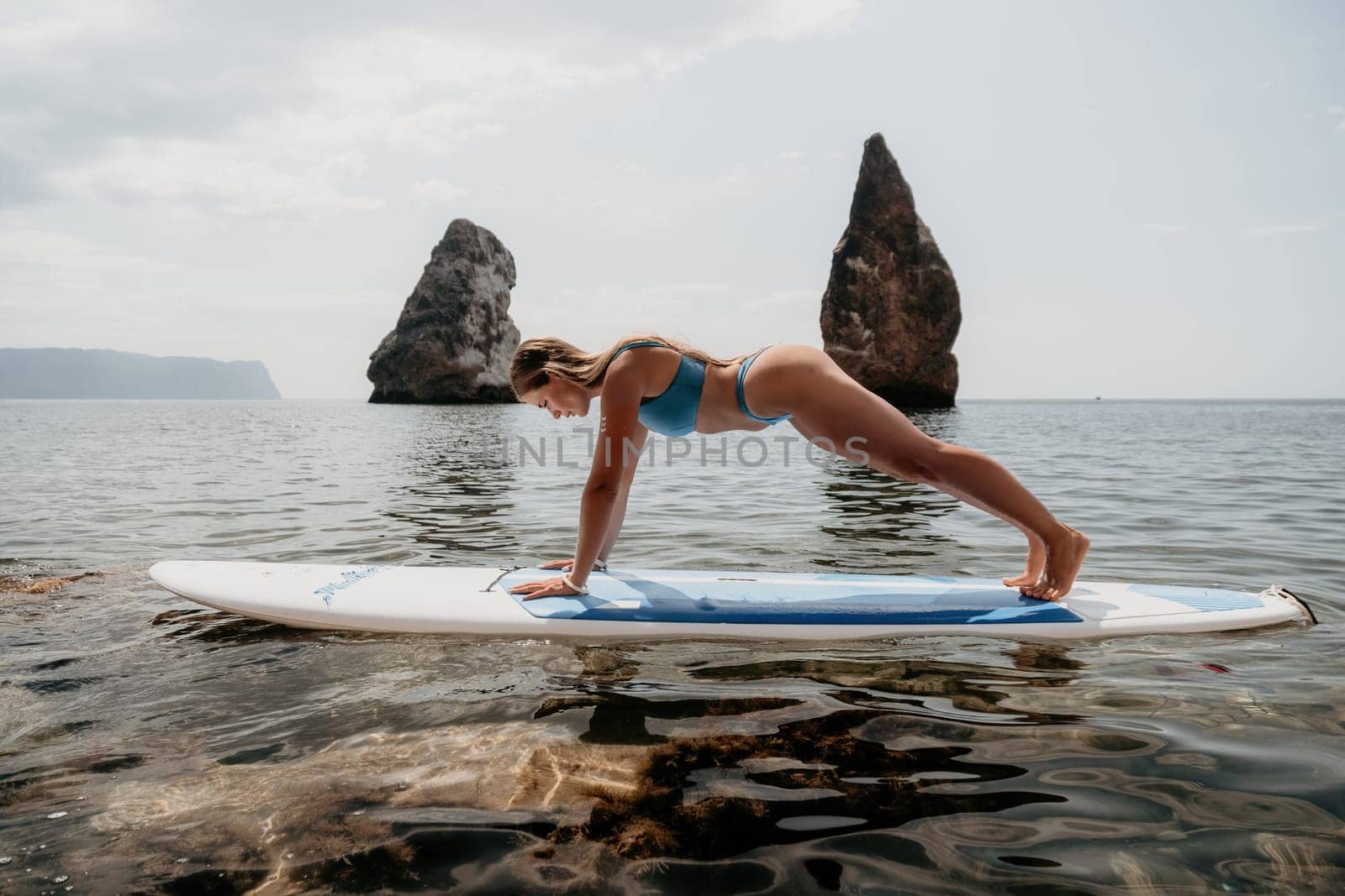 Woman sup yoga. Middle age sporty woman practising yoga pilates on paddle sup surfboard. Female stretching doing workout on sea water. Modern individual hipster outdoor summer sport activity