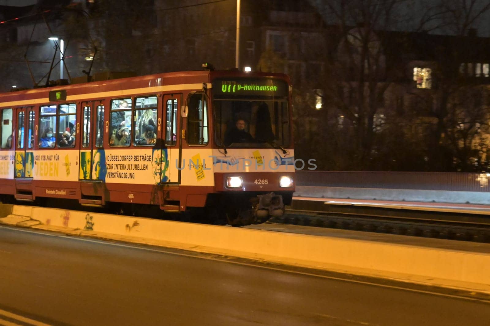 A tram traveling down the track in front of buildings at night