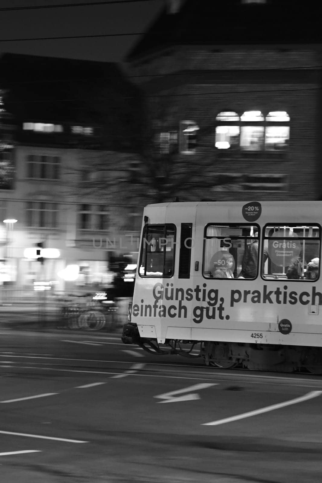Grayscale of a tram going through town streets at night on the street