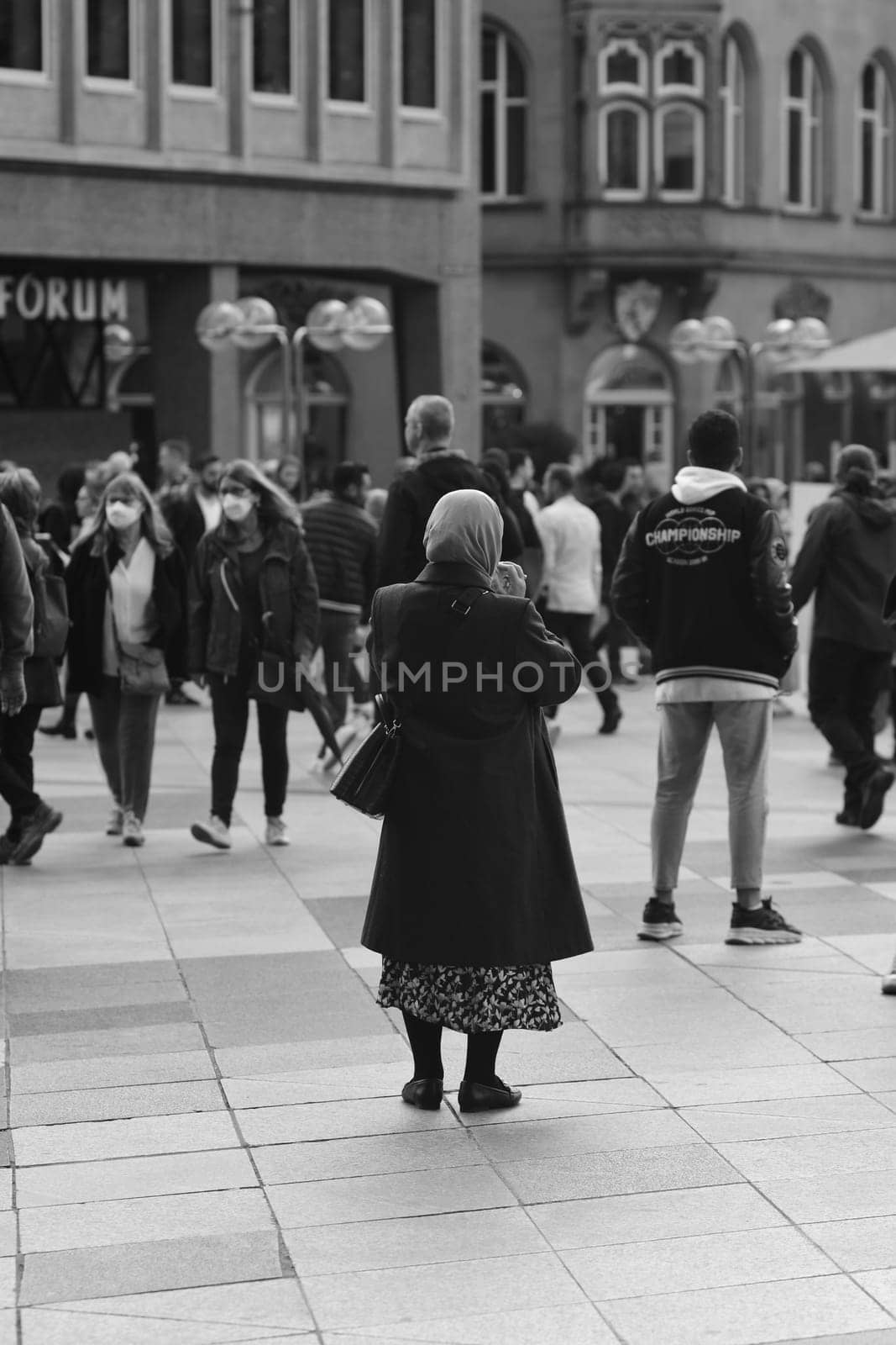 Vertical grayscale of a woman wearing a hijab standing in front of Cologne Cathedral, Germany