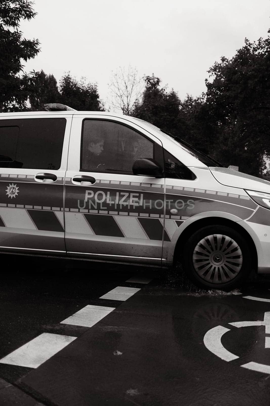 Vertical grayscale of two officers in a German police car on a rainy day in Dusseldorf