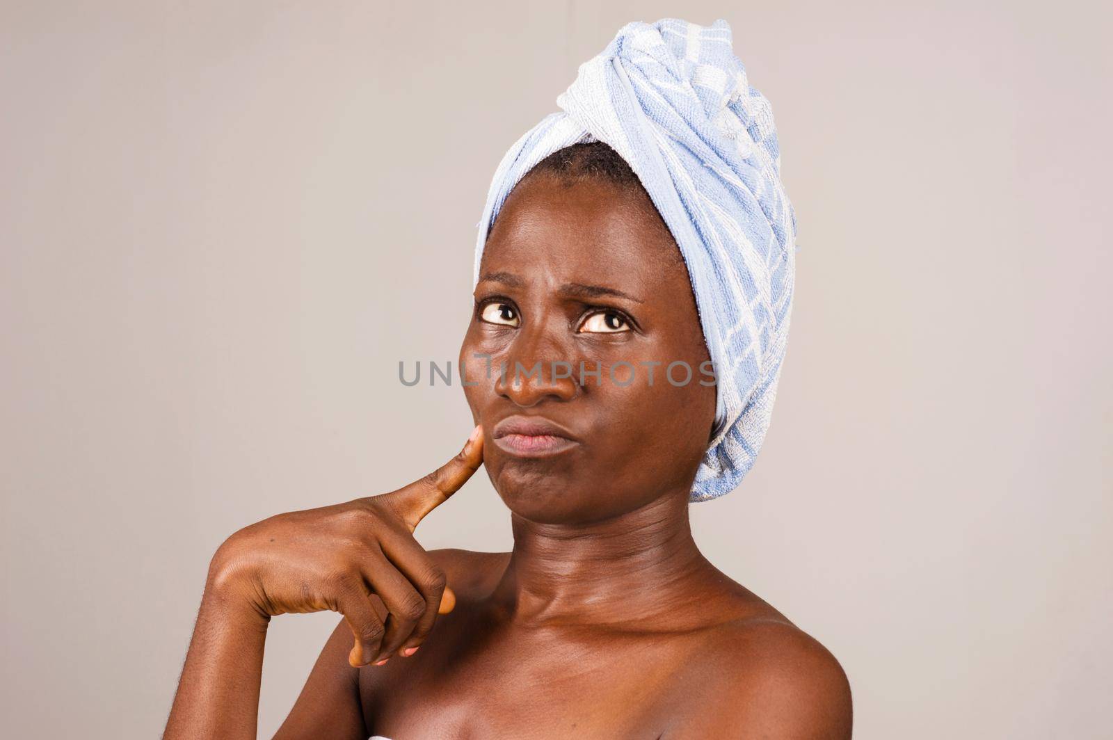 African girl standing on gray background, bath towel knotted on head with air displeased.