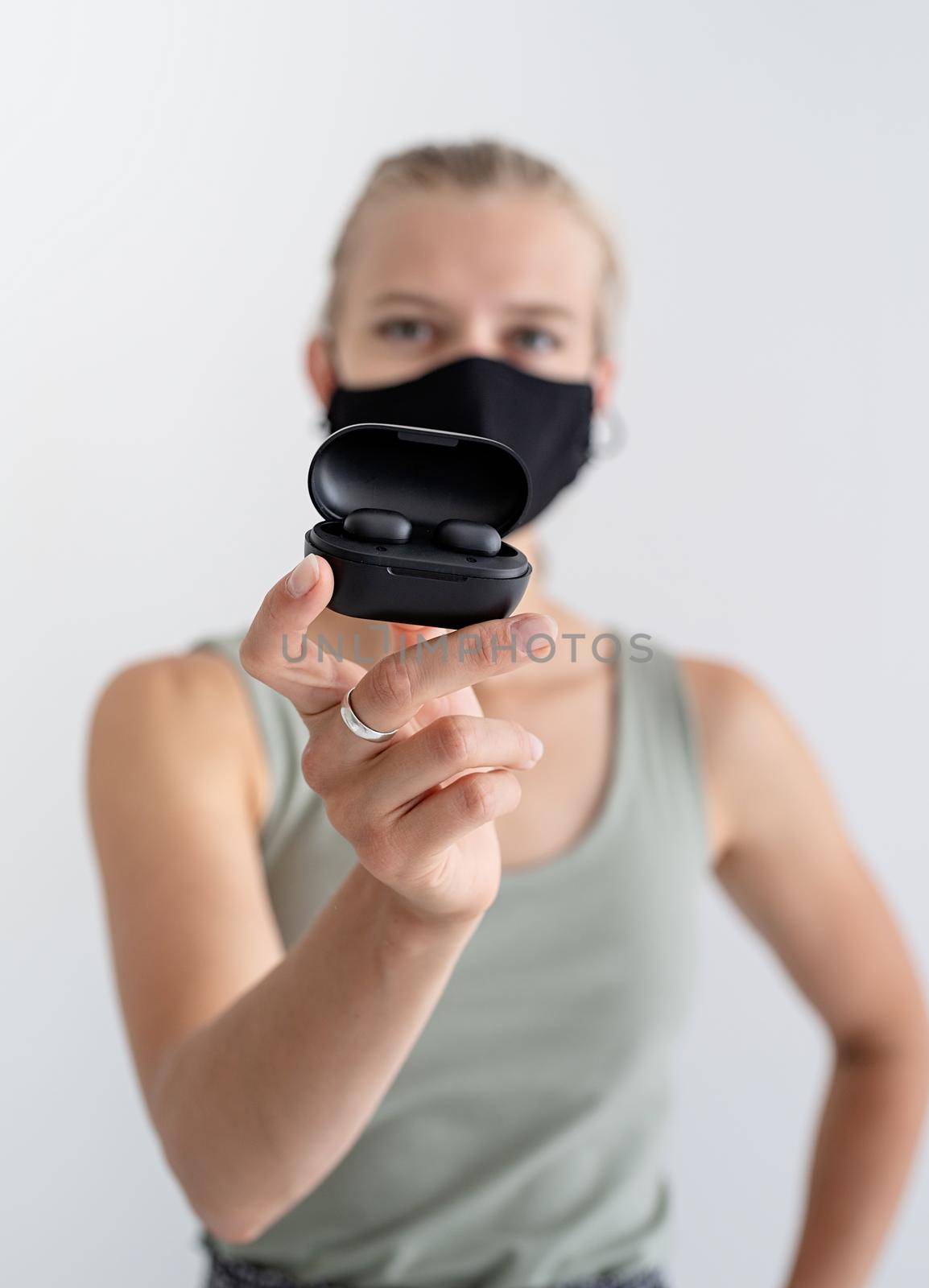 Music, isolation and leisure. Young woman in a protective mask holding wireless earbuds