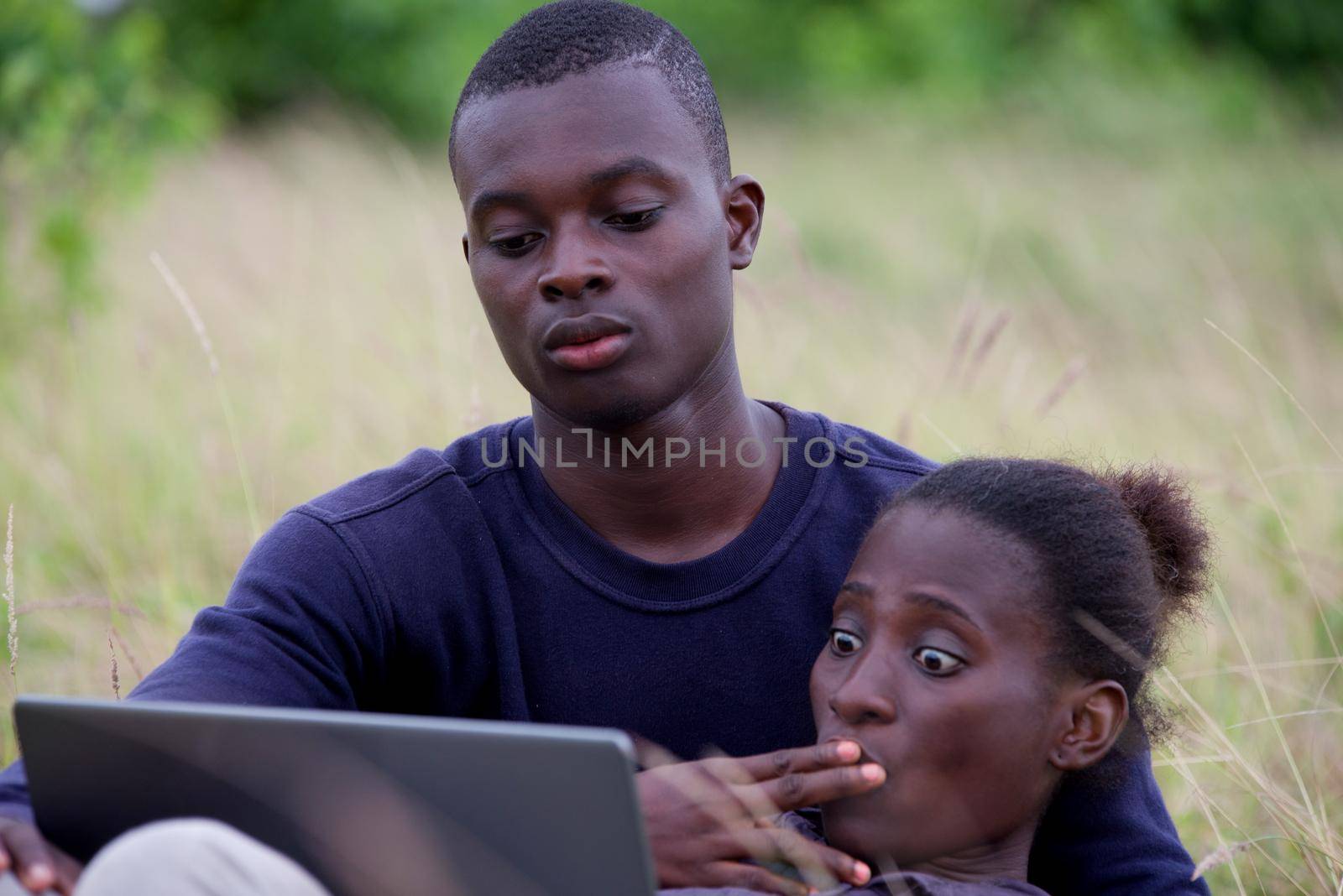 young african couple sitting in the grass with laptop.