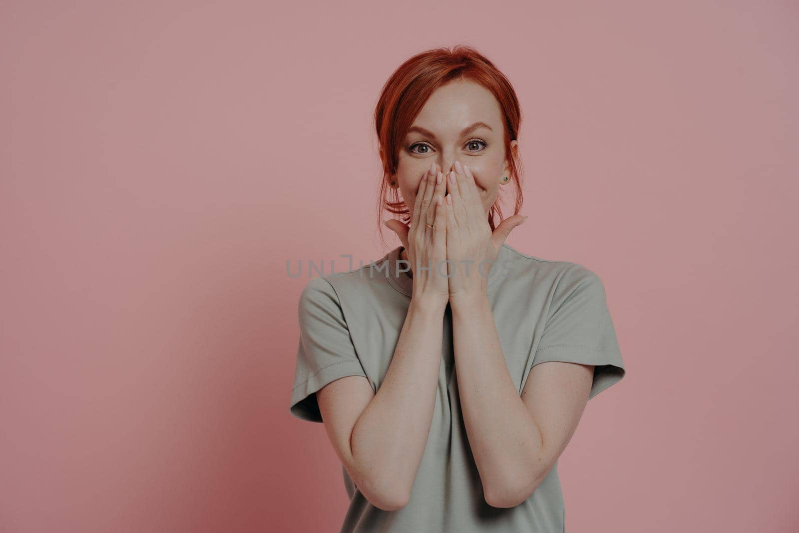 Excited happy red-haired woman covering mouth with hands, looking with surprised facial expression by vkstock