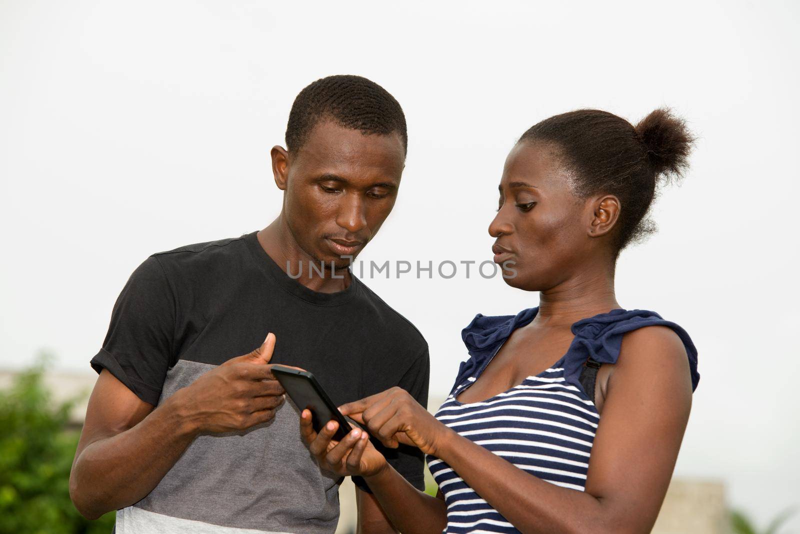 portrait of young african couple standing staring at mobile phone.