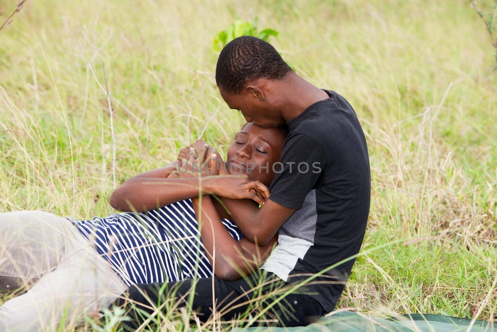 young african couple sitting in a park, intertwined.