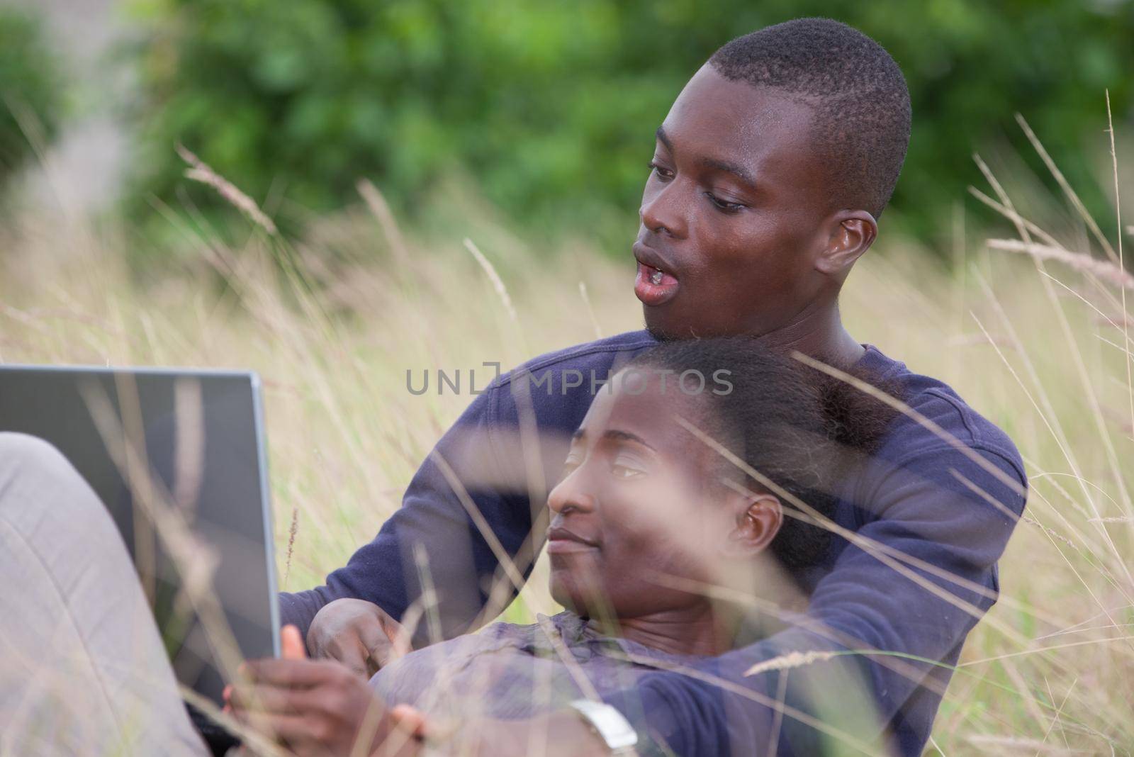 young african couple sitting in the grass with laptop
