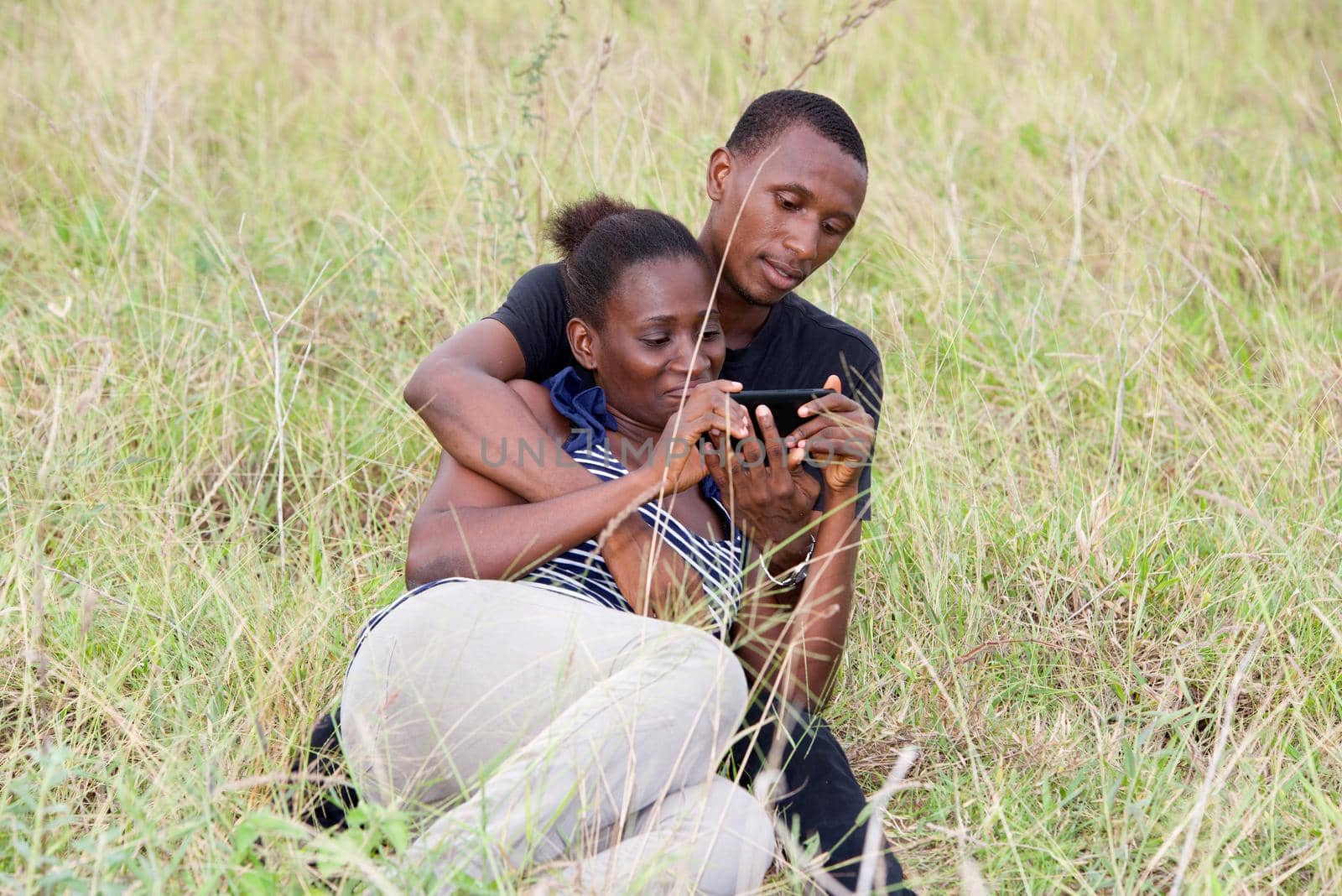 young girl and young man sitting in grass watching mobile phone.