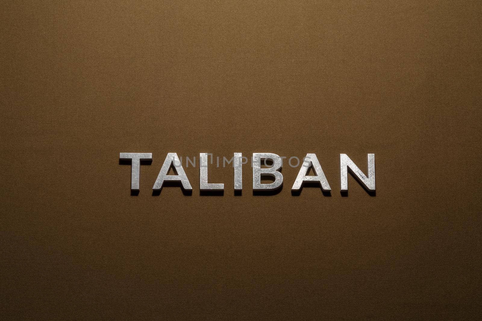 the word taliban laid with silver metal letters on tan khaki canvas fabric