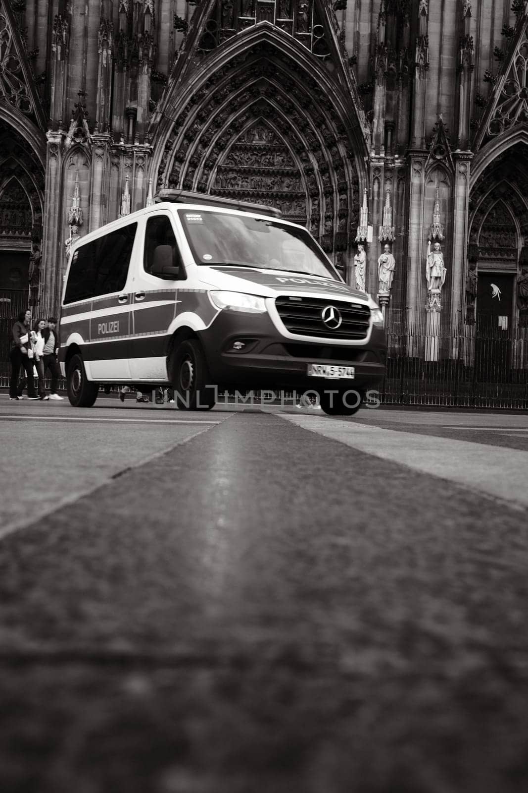 Grayscale shot of Mercedes-Benz Sprinter police car in front of Cologne Cathedral in Germany