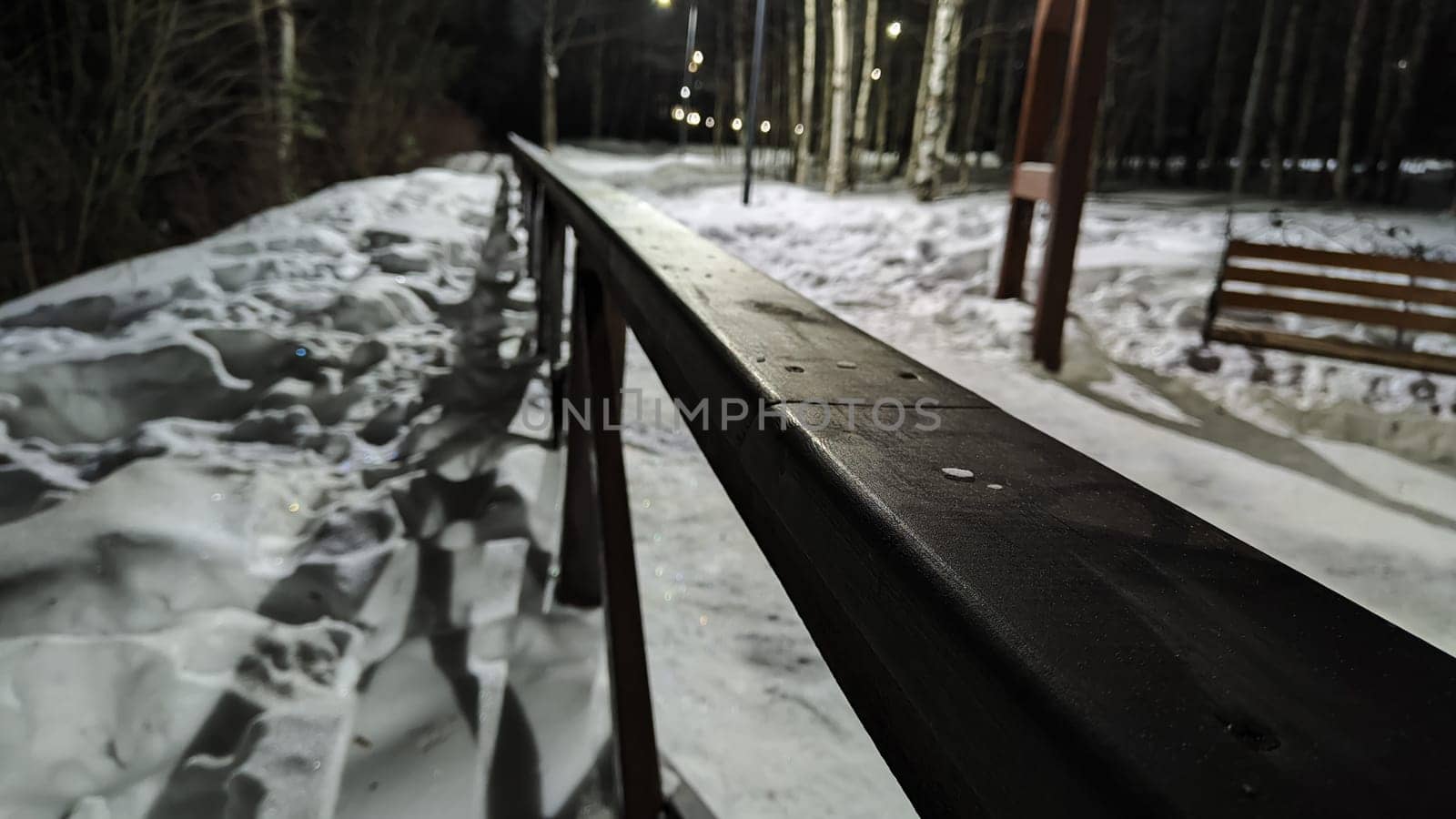 Long black railings on winter night and white snow all around. Partial focus and distant blur