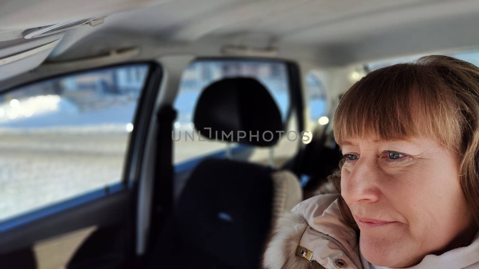 Woman sitting in the car in road trip. Blonde senior Woman driving transport. Lady travelling in cold time