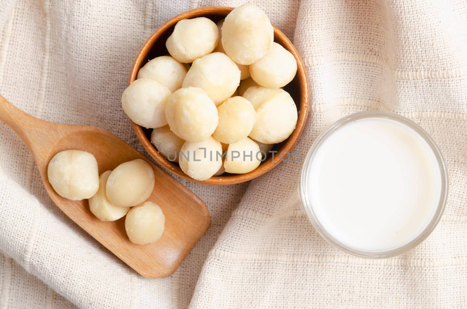 Macadamia milk in glass and a bowl of macadamia on tablecloth.