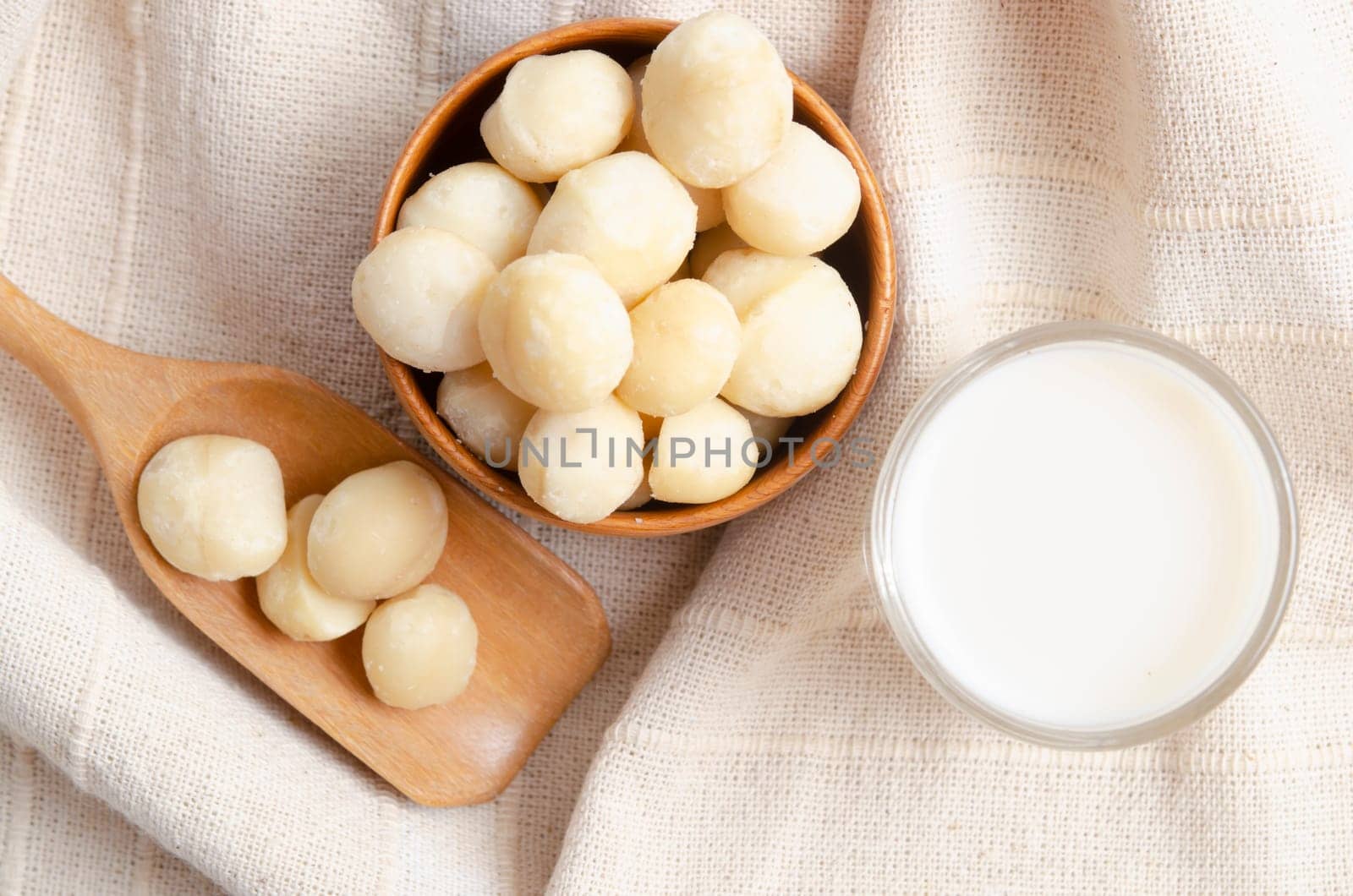 The Macadamia milk in glass and a bowl of macadamia on tablecloth. by Gamjai