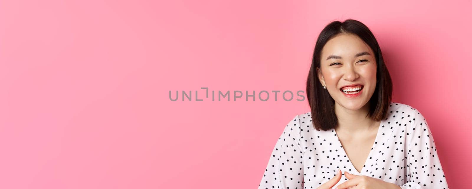 Beauty and lifestyle concept. Close-up of happy asian woman laughing and having fun, standing over pink background by Benzoix