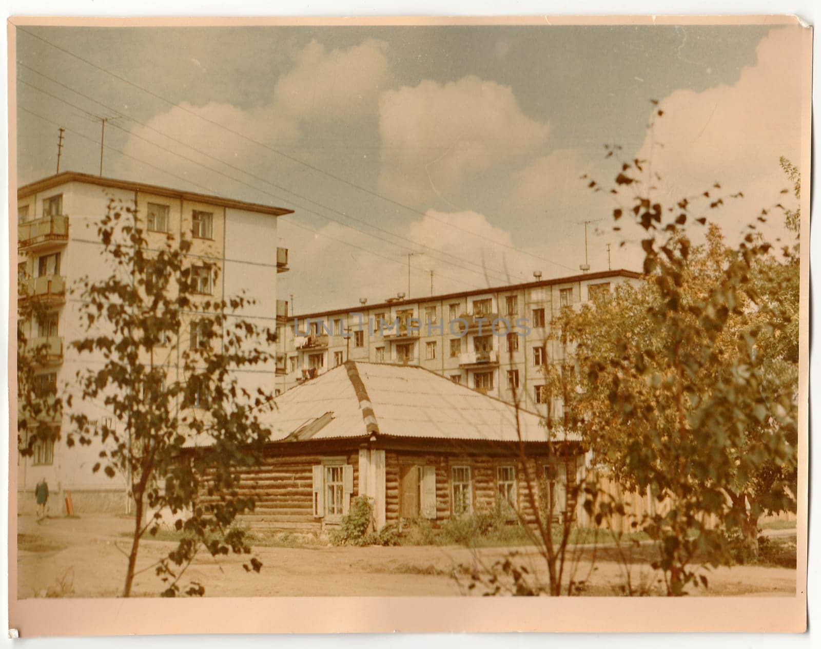 Vintage photo shows log cabin (log house) and blocks of flats in the background. by roman_nerud