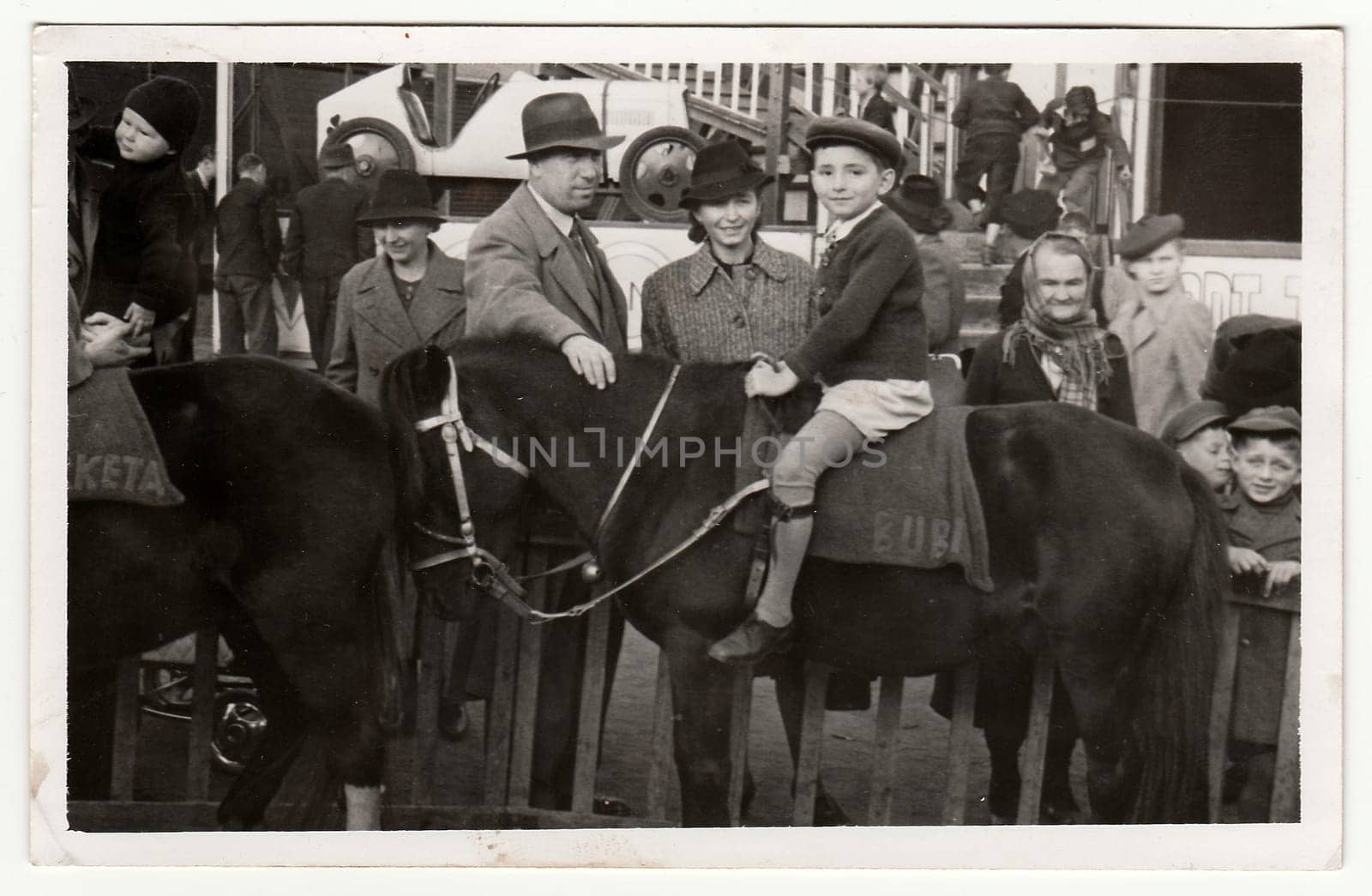 Vintage photo shows family in amusement park. A small boy sits on horse. by roman_nerud