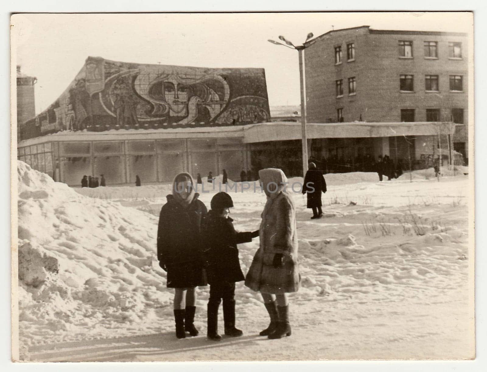 Vintage photo shows girls and boy talk on street in winter. Socialist mosaic on background. by roman_nerud