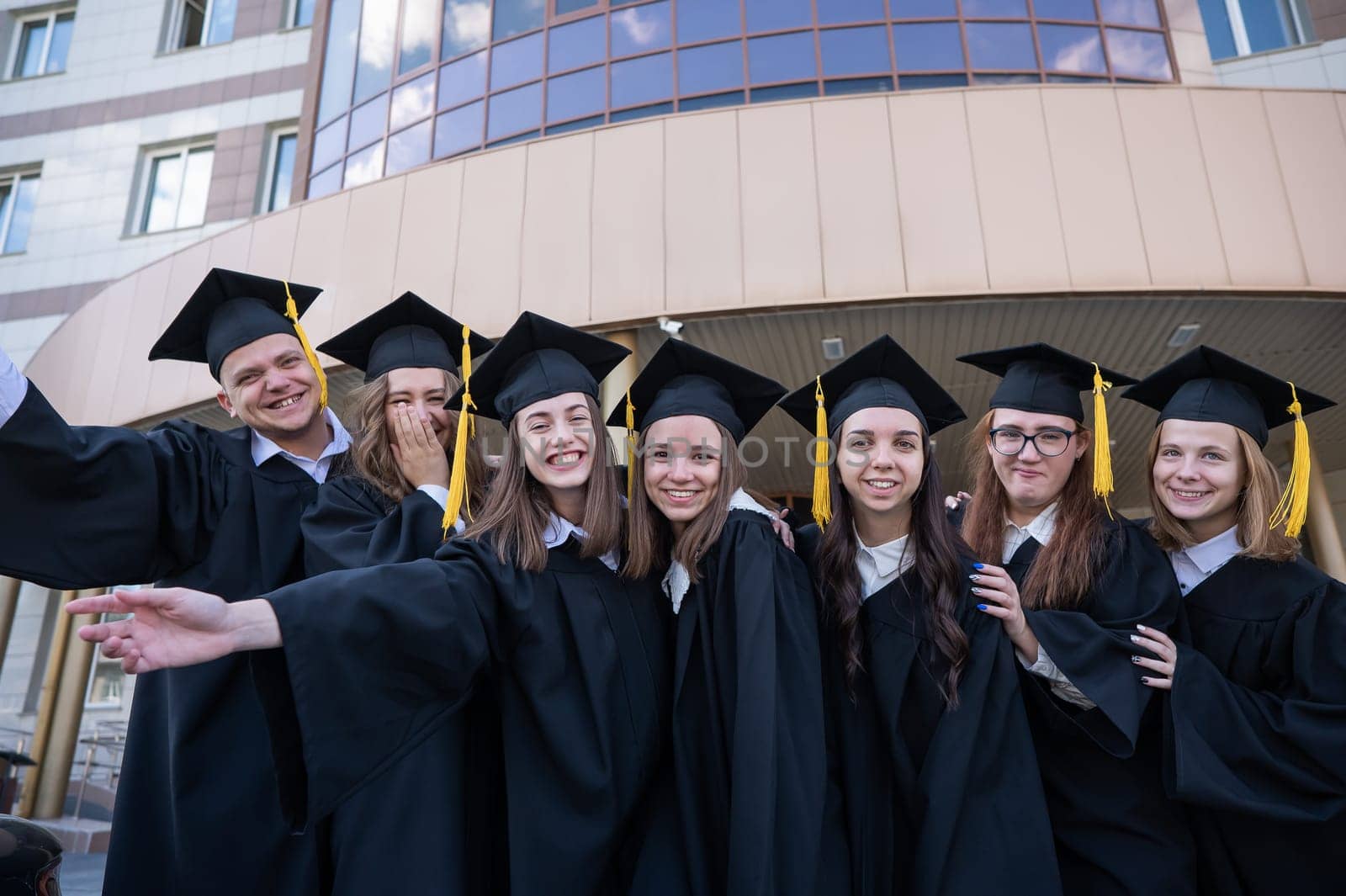 Happy students in graduate gown stand in a row against the backdrop of the university