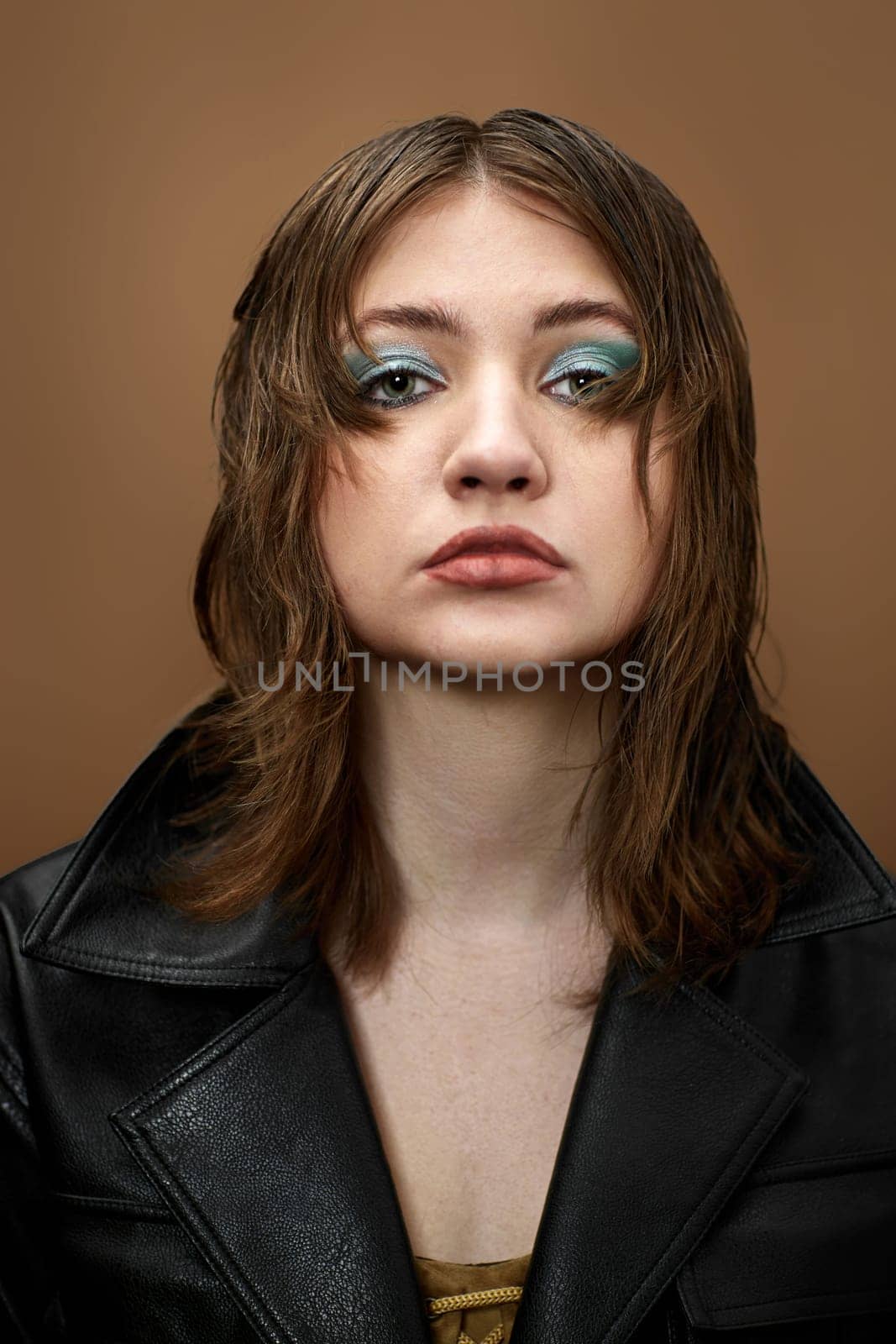 young woman with bright makeup and stylish hairstyle in black jacket on beige background.