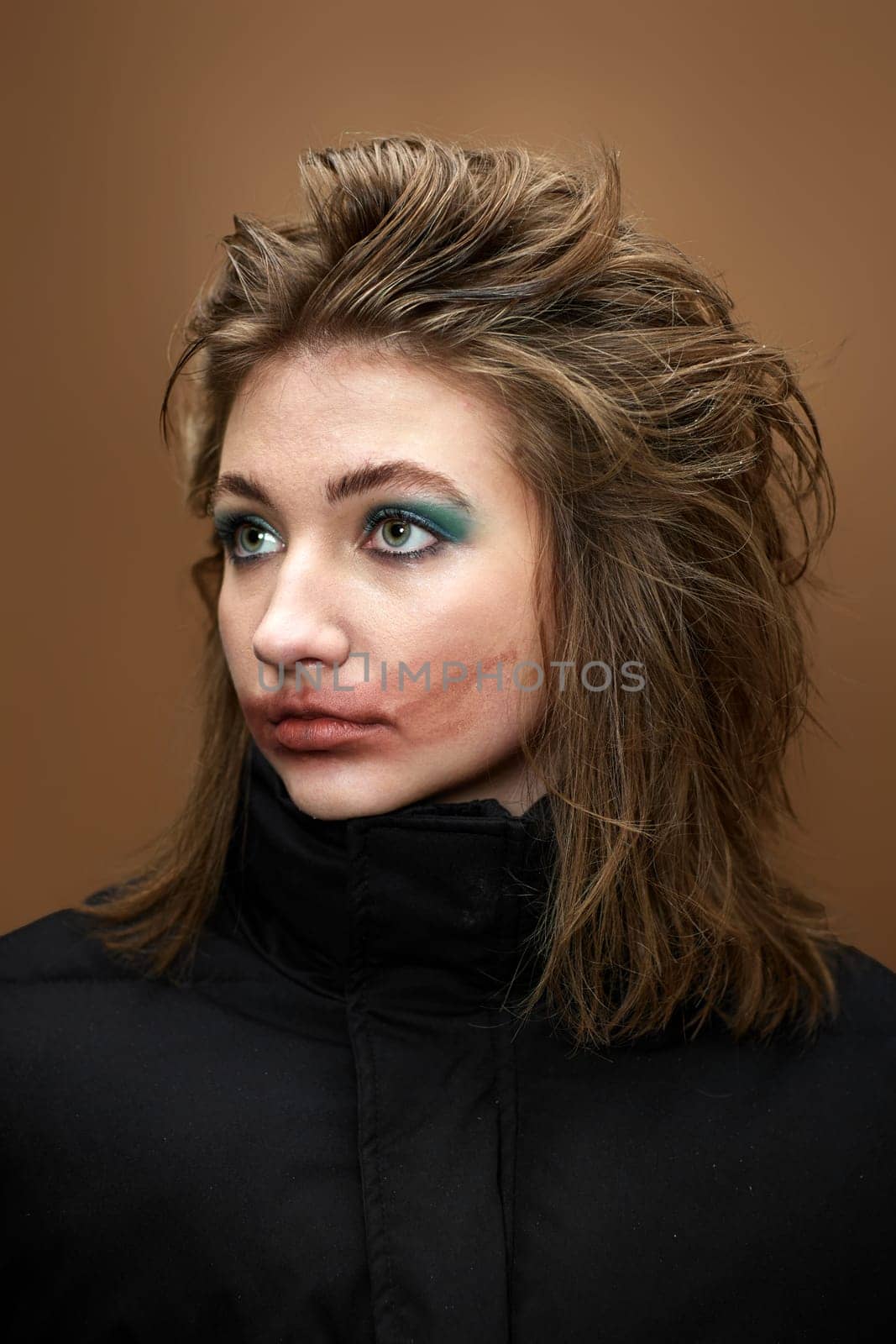 portrait of woman with smudged lipstick and stylish hairstyle in black jacket on beige background.