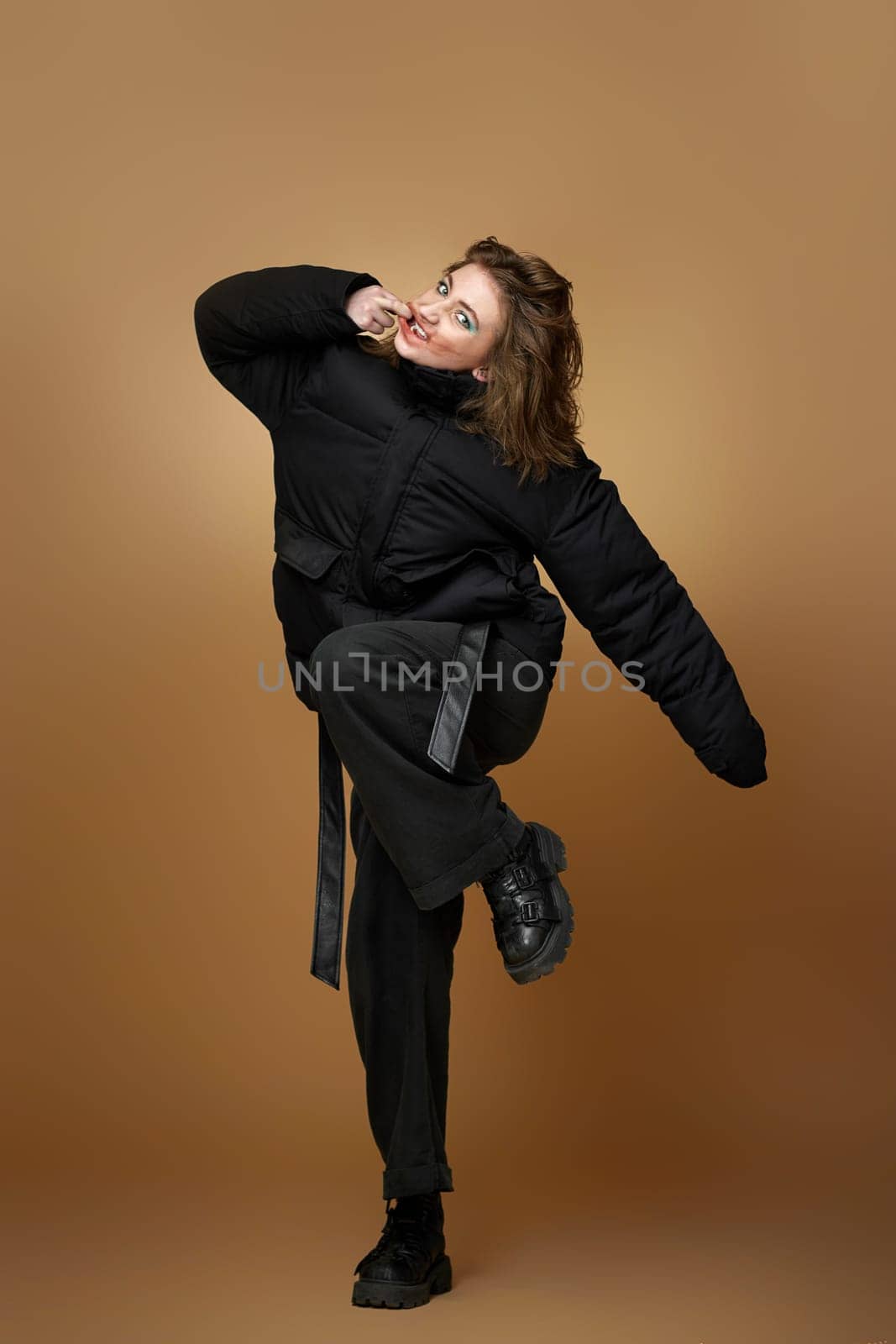 young stylish woman with bright makeup posing in black jacket and pants on beige background. total black look