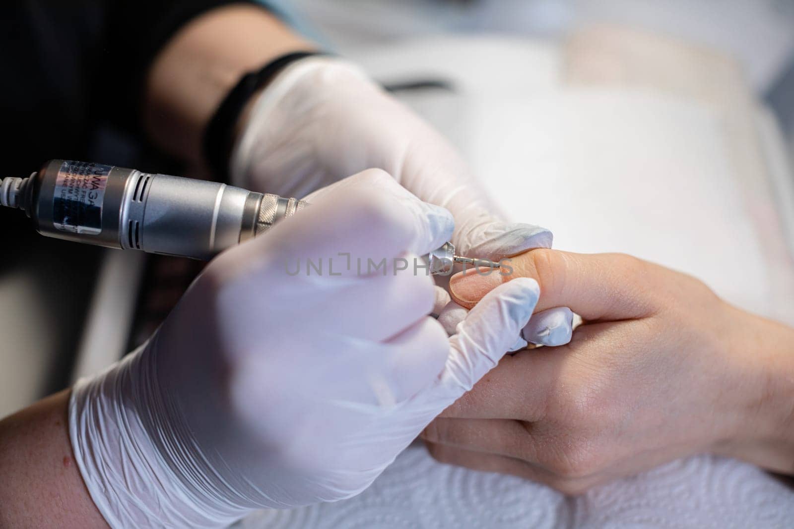 A beautician at a beauty salon wears disposable gloves. A woman undergoes a service at a professional salon. The beautician performs a manicure on the natural nail plate.