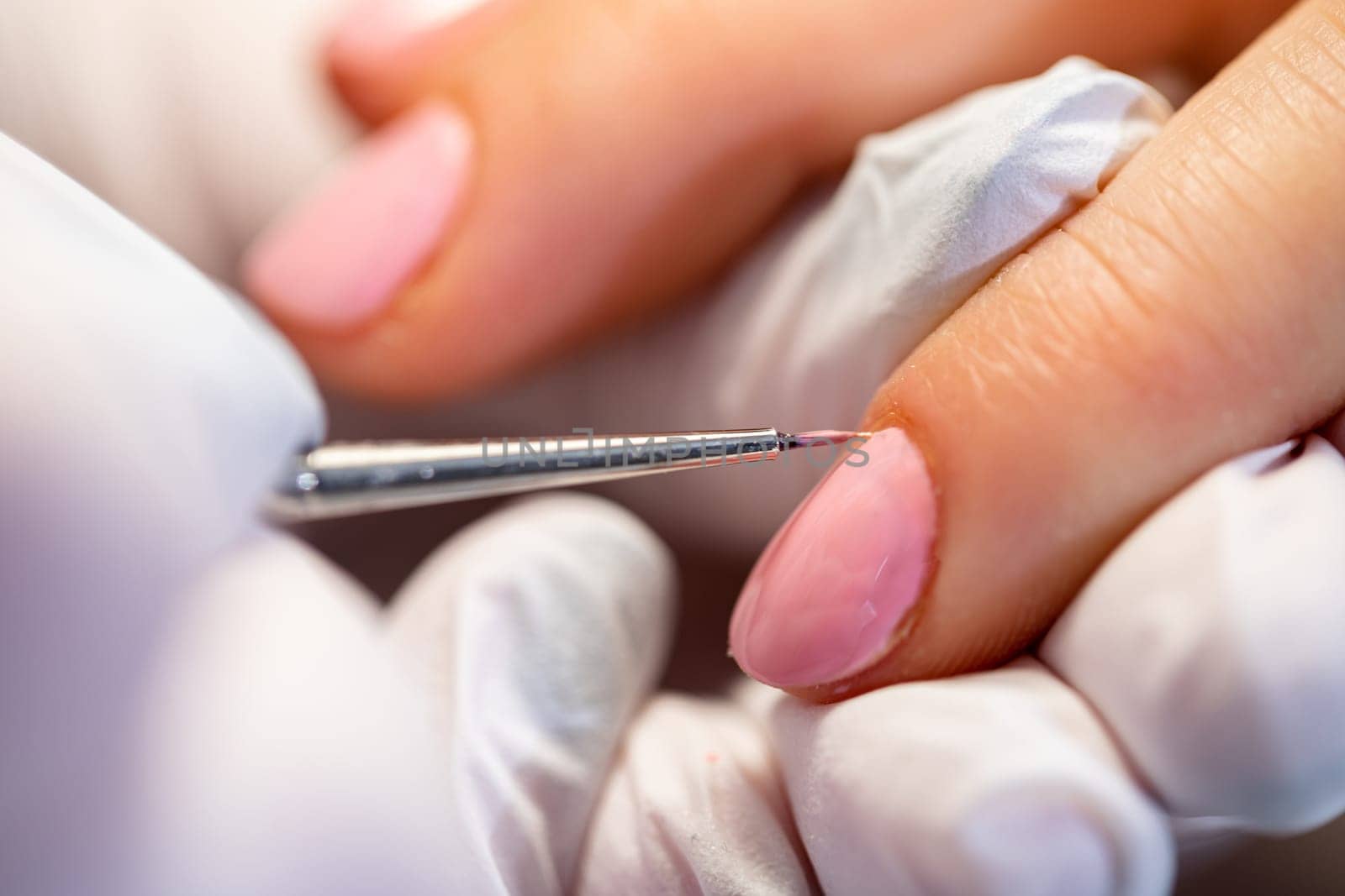 A beautician applies hybrid polish to a client's nails. Professional customer service. Precise nail painting in a beauty salon. Taking care of the nail plate.
