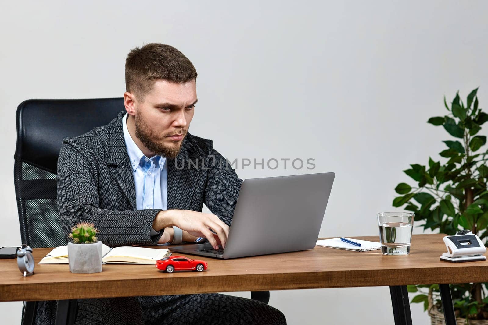 young bearded businessman typing on computer keyboard, sending emails to business partners, sitting on chair at desk