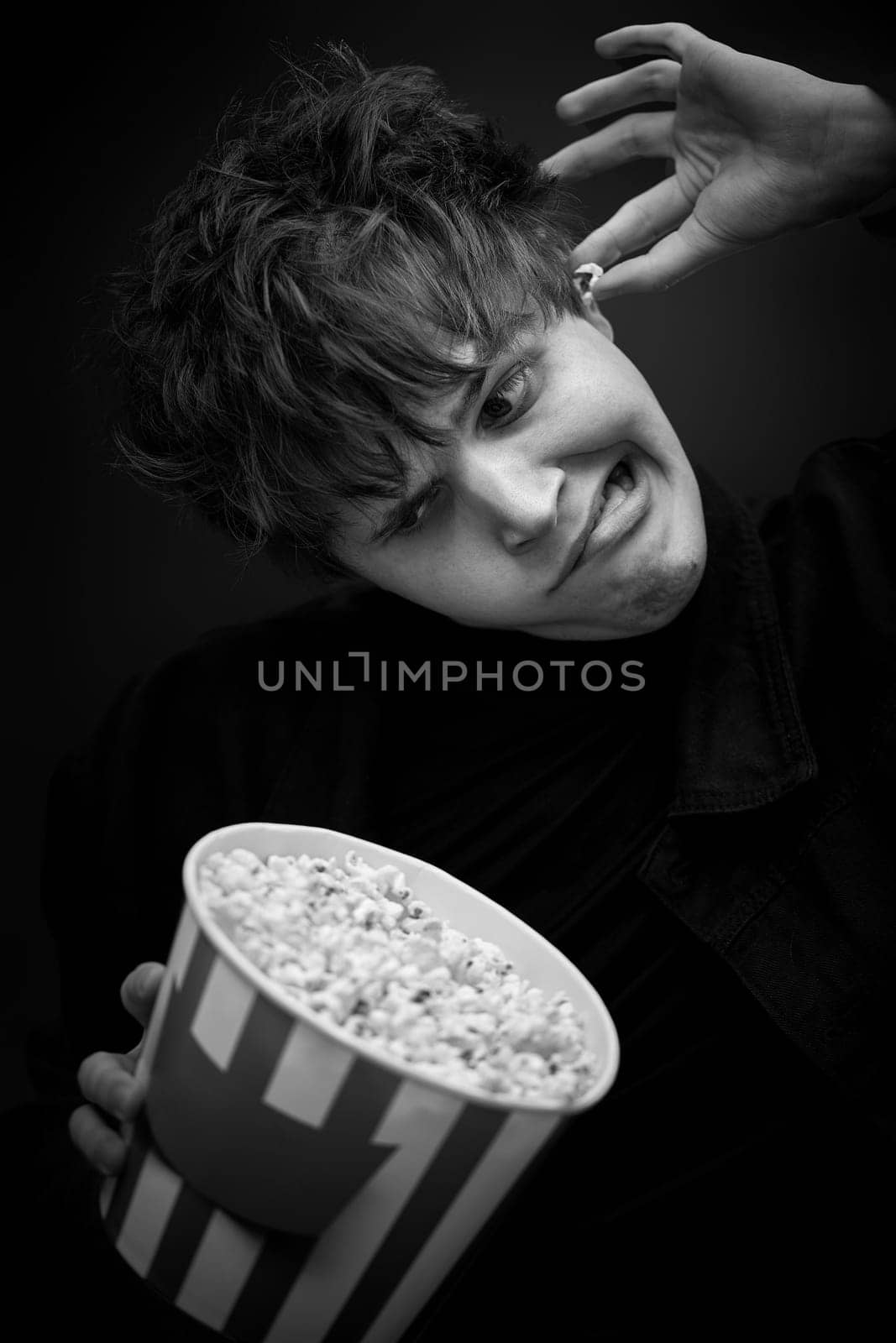 portrait of crazy young man holding bucket of popcorn and grimacing . black and white