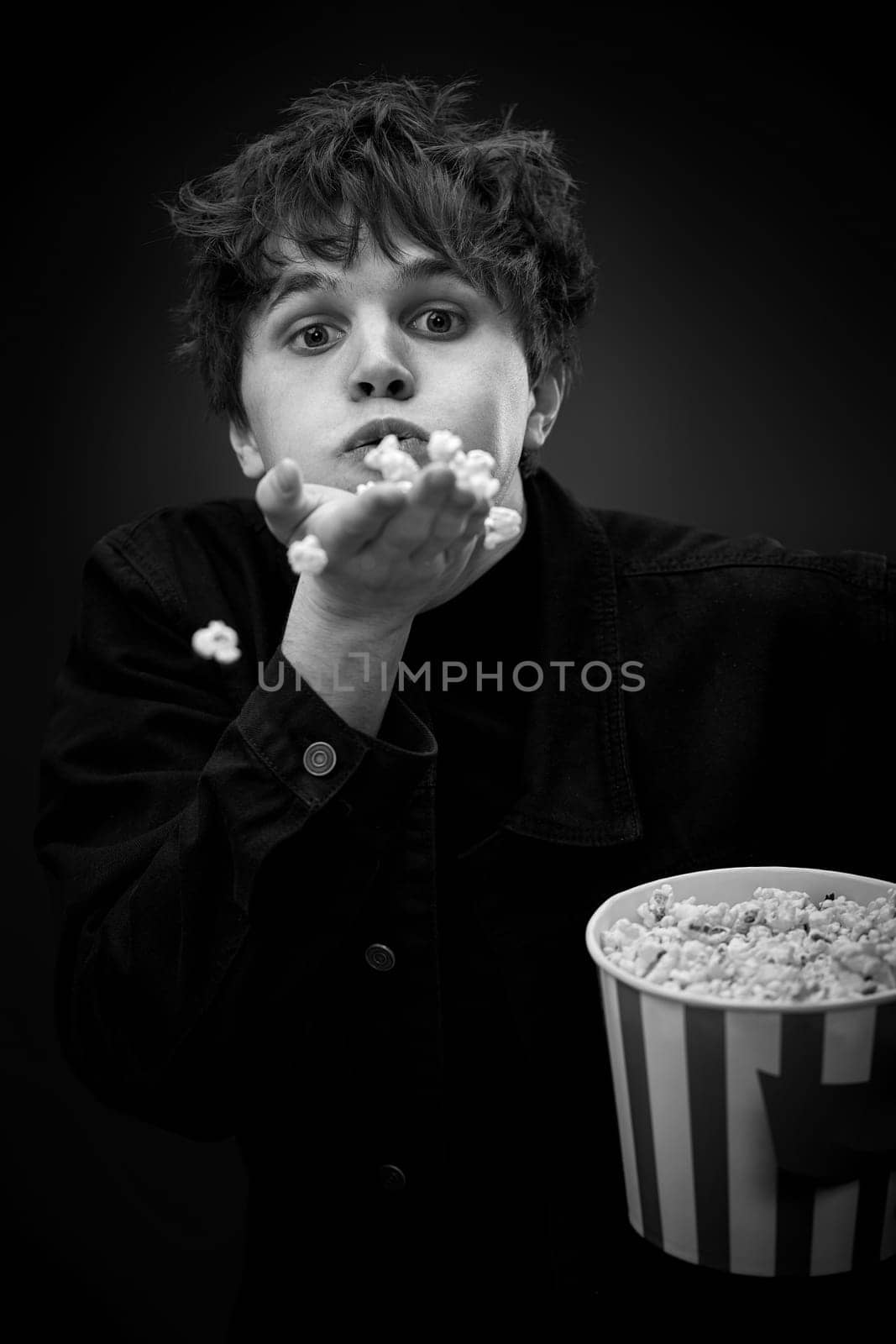 portrait of crazy young man throwing up popcorn and grimacing . black and white