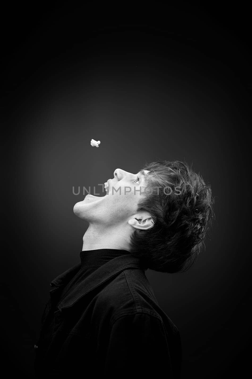 side view of crazy young man throwing up popcorn and grimacing . black and white