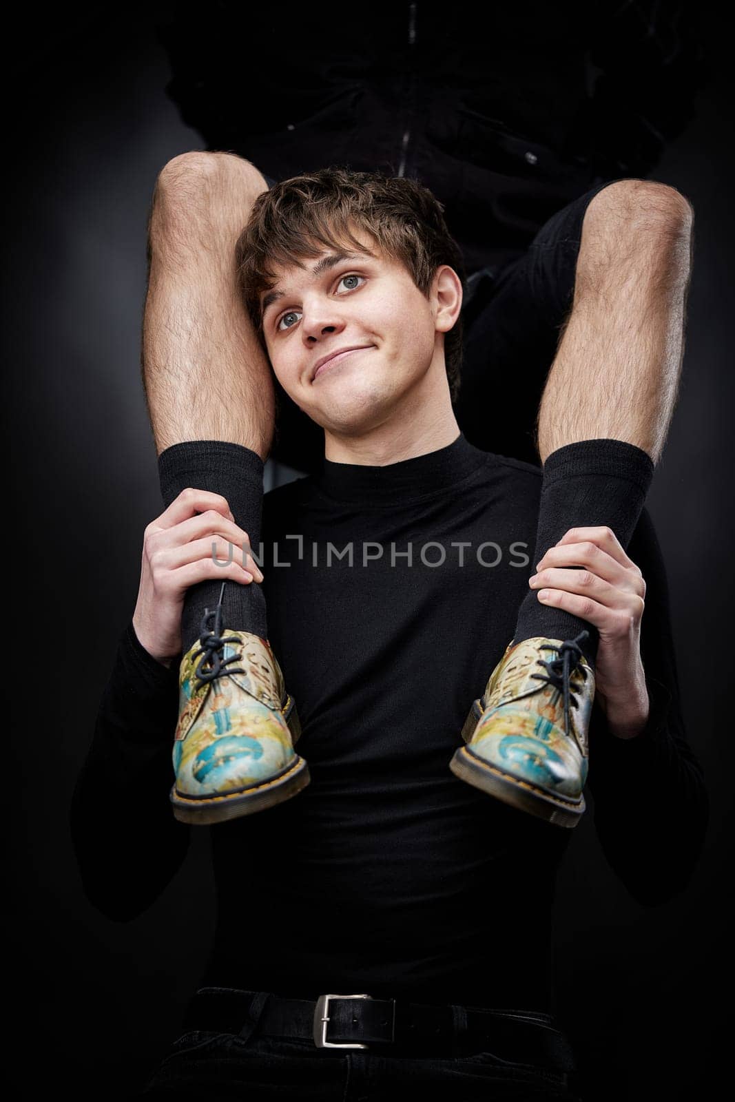 young handsome guy hugs male legs in bright shoes on black background. fashion