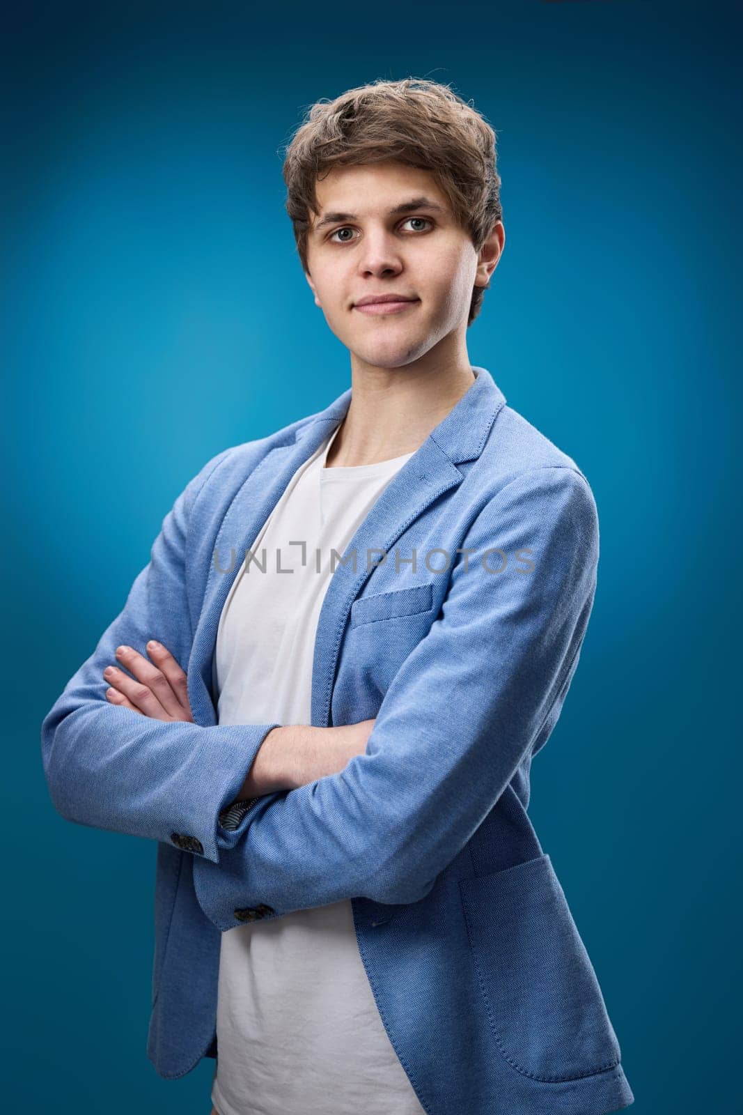 young guy in jacket posing with crossed arms and looking at the camera on blue studio background