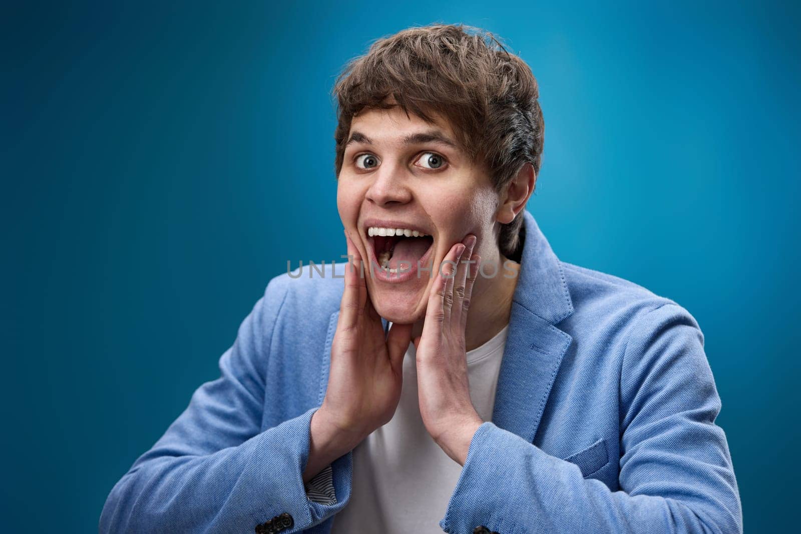 happy shocked man with surprise expression and excited face on blue studio background