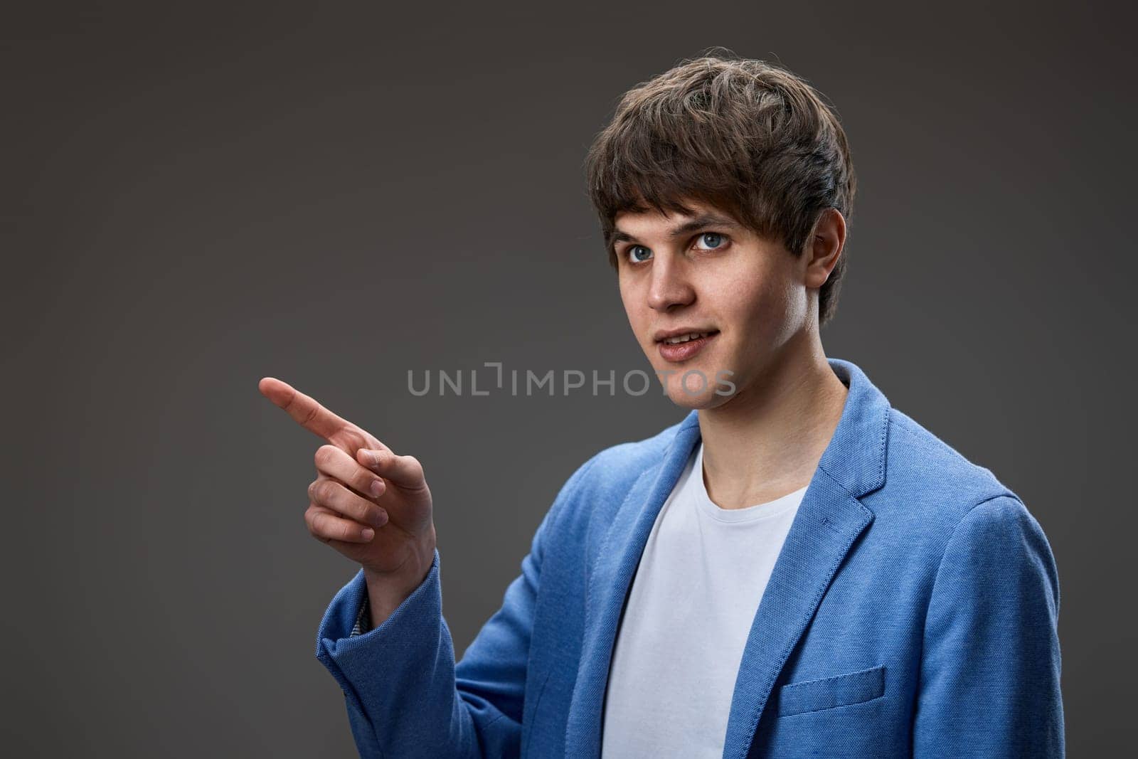 handsome caucasian young man in jacket pointing finger at empty space on gray background