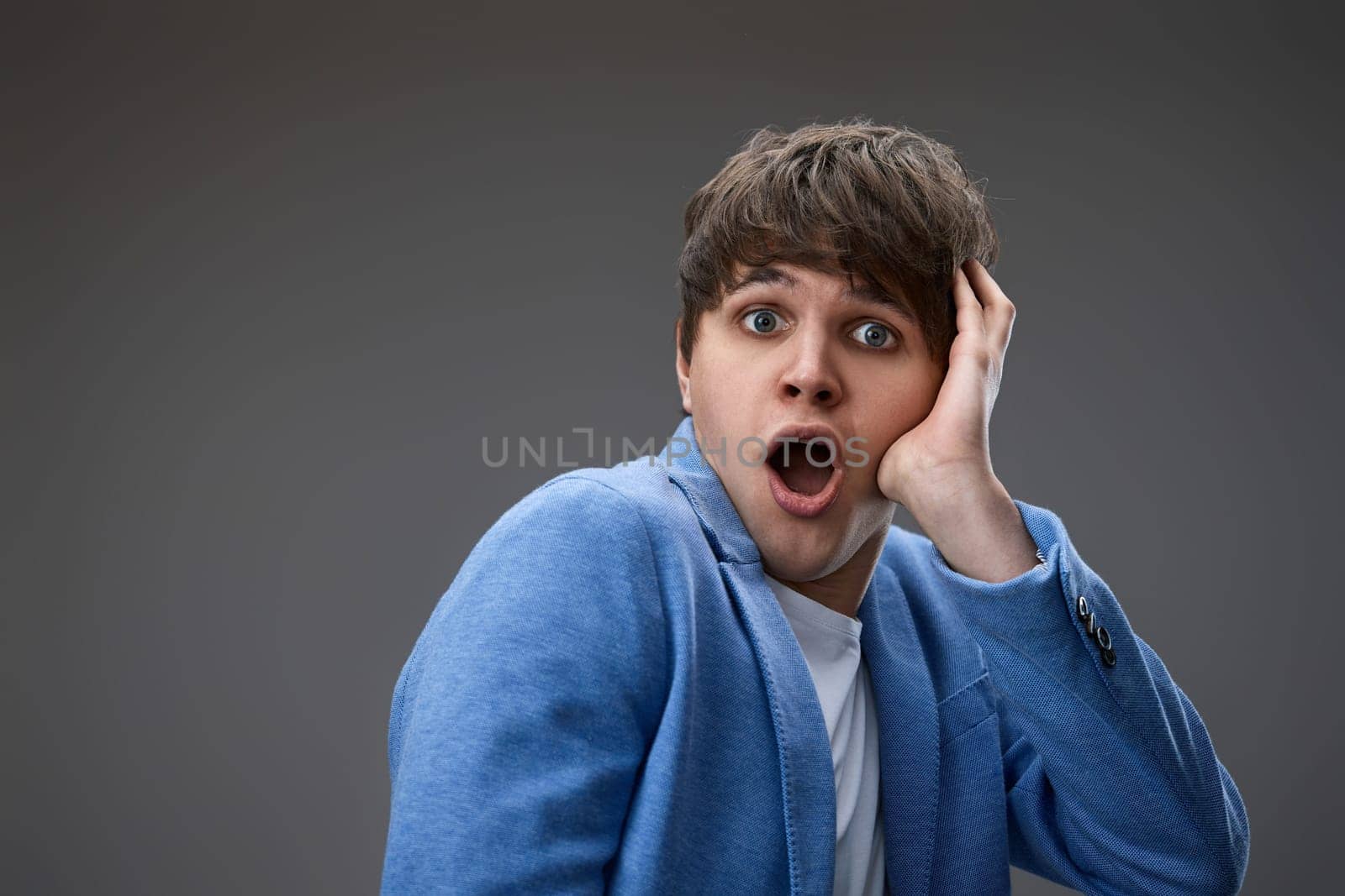 shocked man with surprise expression, fear and excited face on gray studio background. close-up