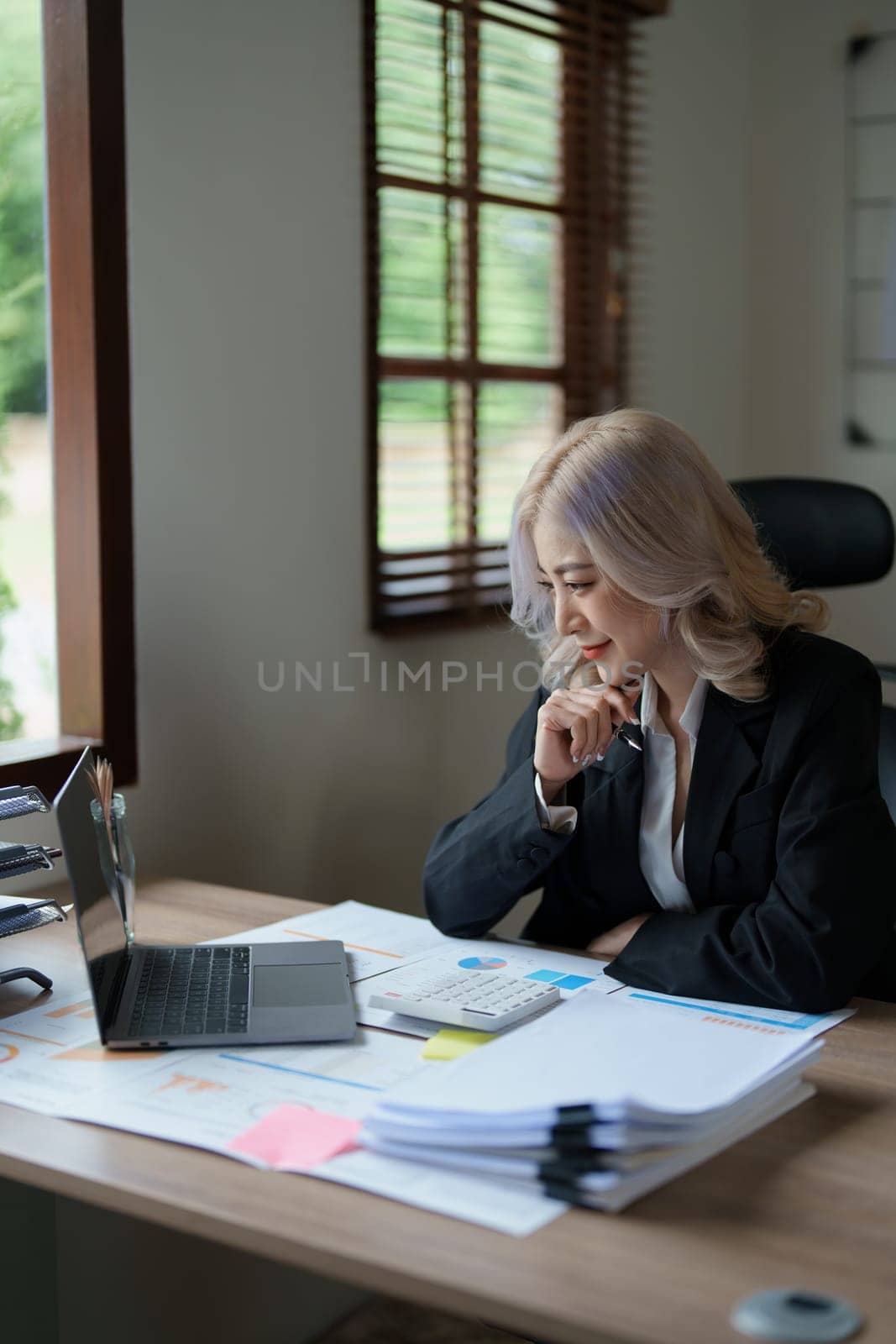 Portrait of a thoughtful Asian businesswoman looking at financial statements and making marketing plans using a computer on her desk.