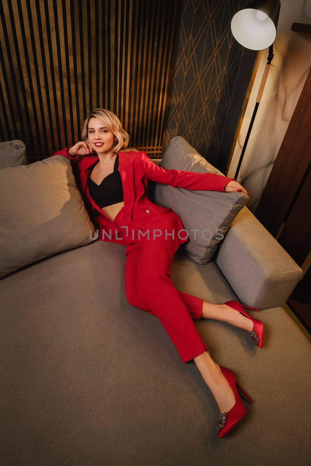 a beautiful girl dressed in a red formal suit posing in a modern interior.