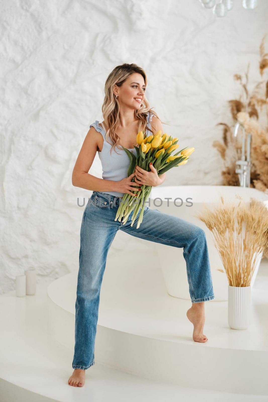 Cute smiling girl with a bouquet of yellow tulips in the interior by Lobachad