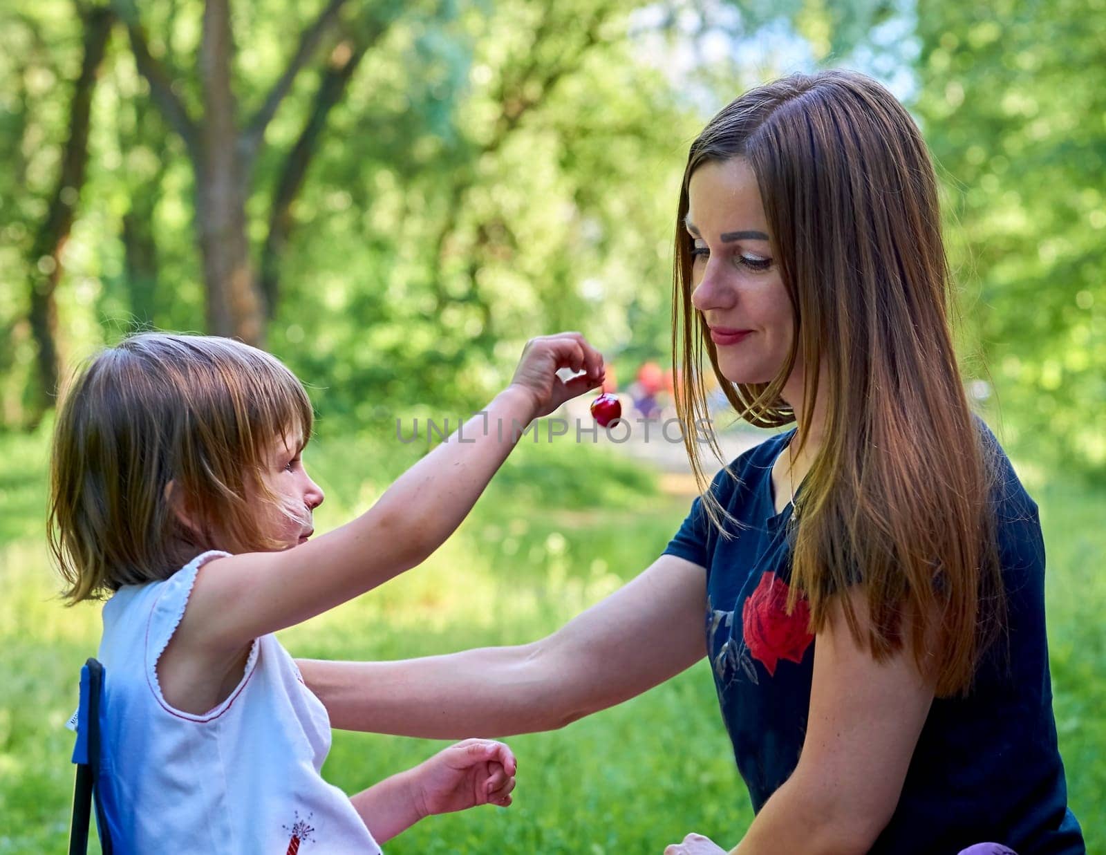 A cute child treats his beloved mother with a sweet cherry berry in nature by jovani68