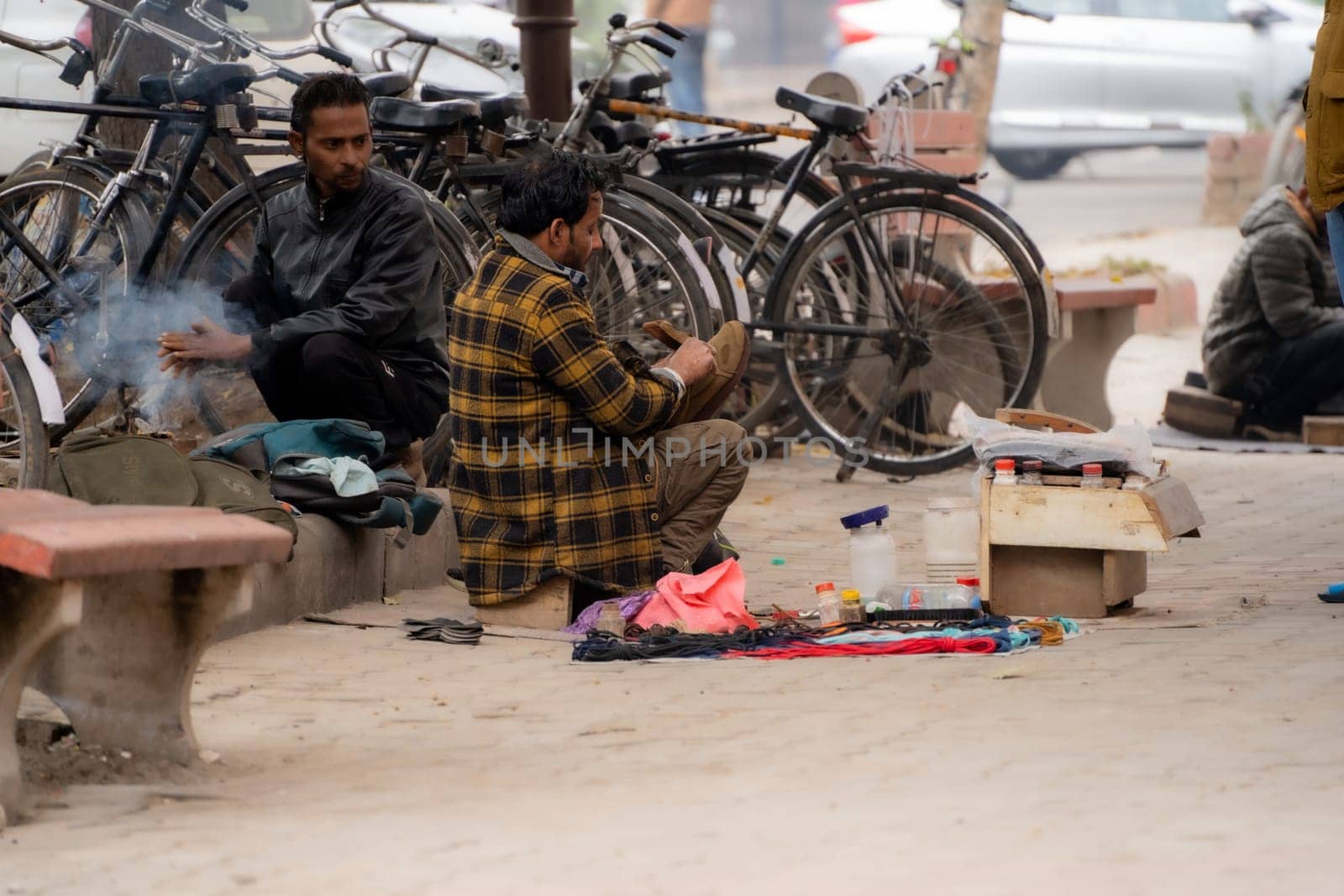 Chandigarh, India - circa 2023 : street side cobbler sitting on road and mending shoes in the winter months in sector 17 chandigarh during morning showing how the poor earn a living