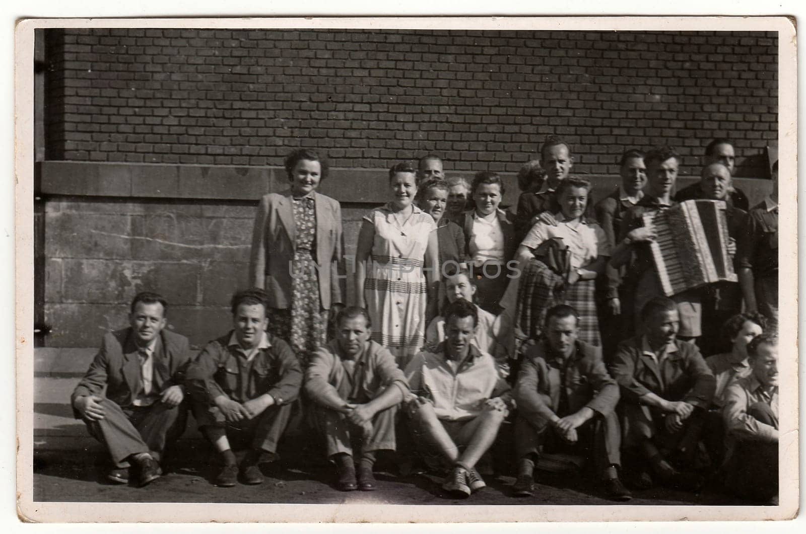 A vintage photo shows group of people, one of them plays the button accordion. Antique black & white photo. by roman_nerud