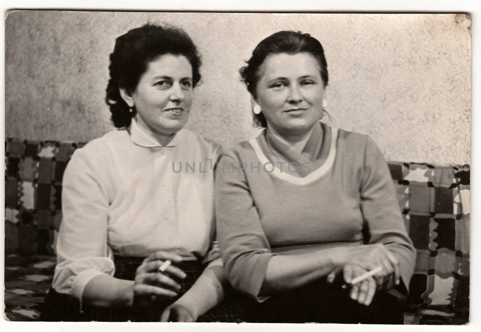 BRNO, THE CZECHOSLOVAK SOCIALIST REPUBLIC - CIRCA 1960s: Vintage photo shows women smoke cigarettes and they sit on the sofa